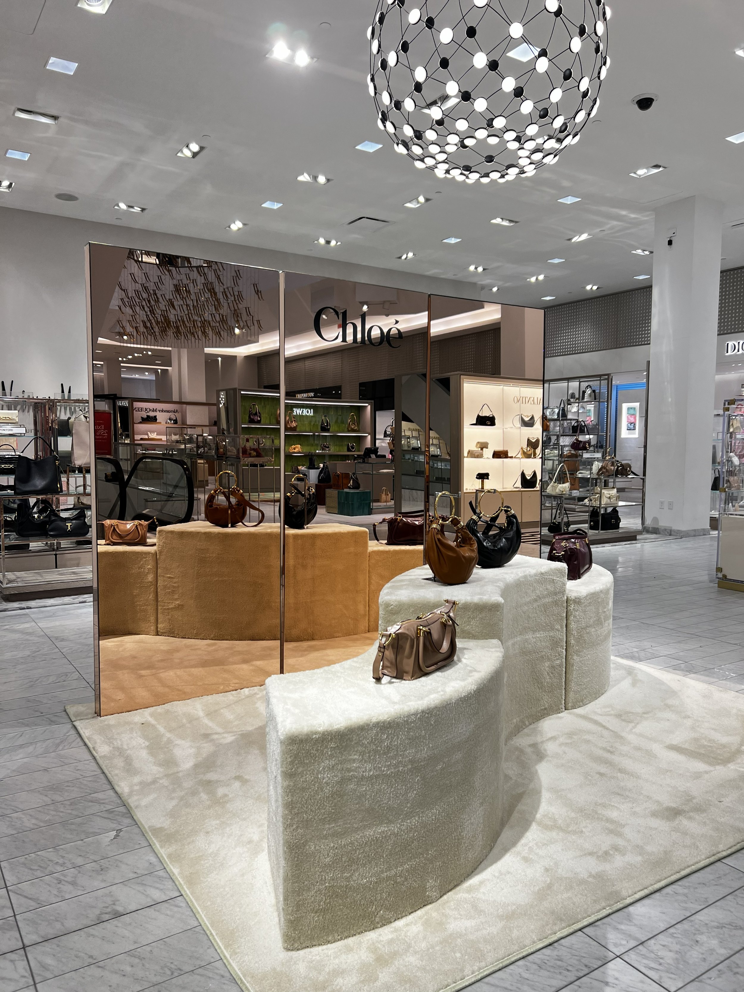 A display of handbags at a luxury boutique store with a chandelier hanging from the ceiling.