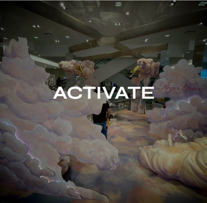 An indoor space decorated with pastel-colored cloud art and clouds hung from the ceiling, featuring a large white and pink cloud installation and a person walking through the area.