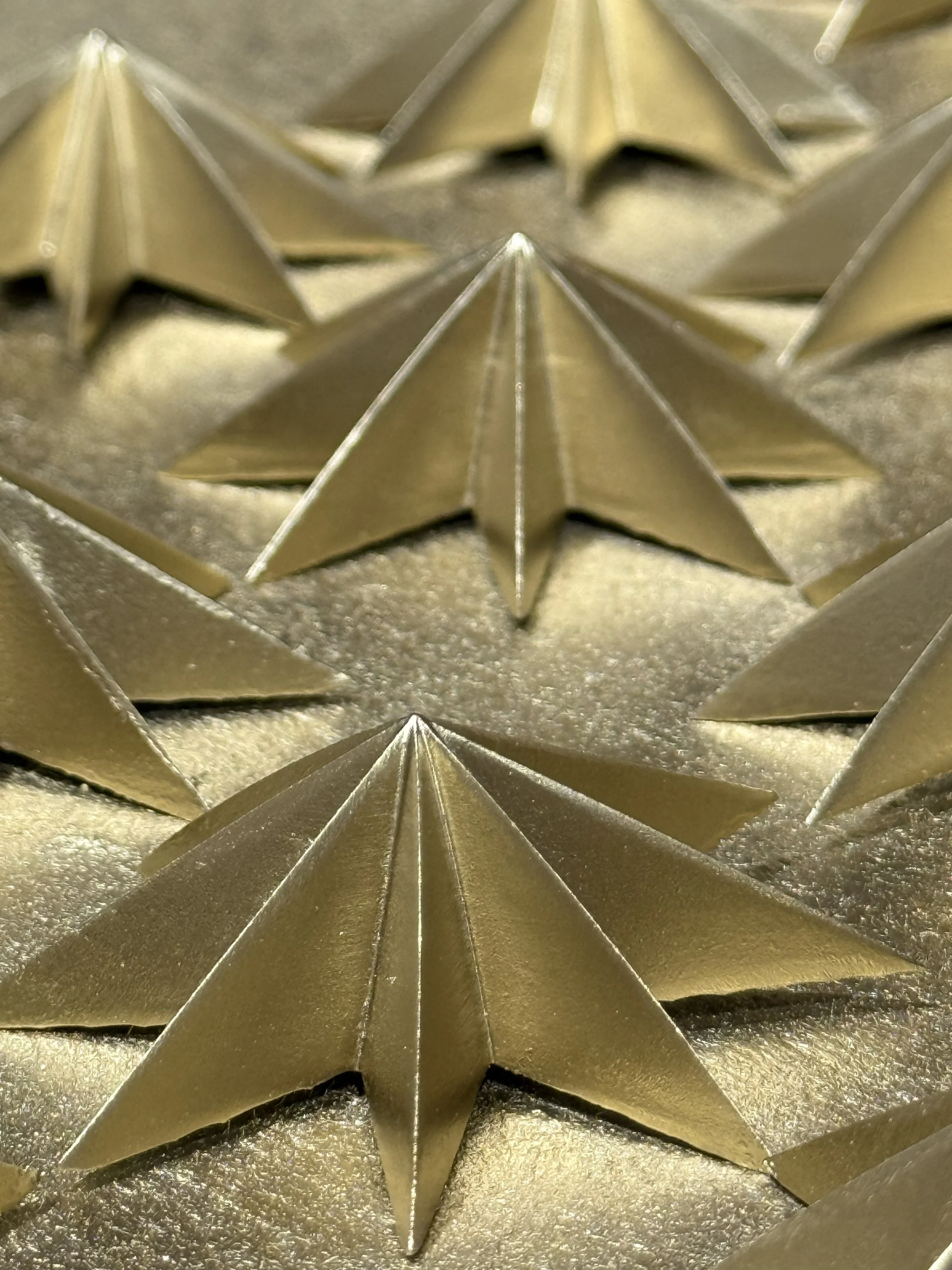 Close-up of shiny gold star-shaped decorations with pointed tips, arranged closely together.