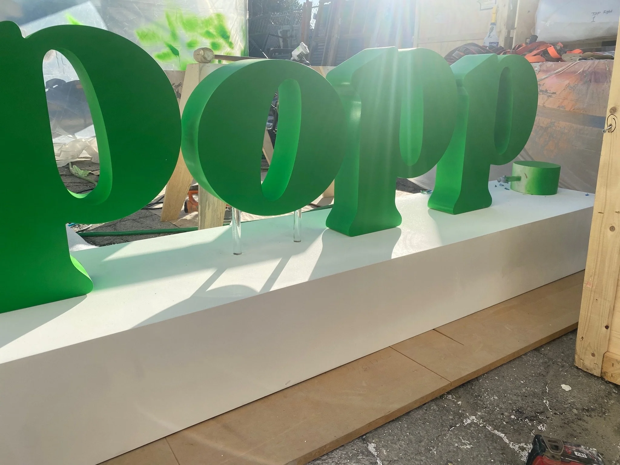 Large green three-dimensional letters spelling 'hope' placed on a white platform, with a workshop and sunlight in the background.