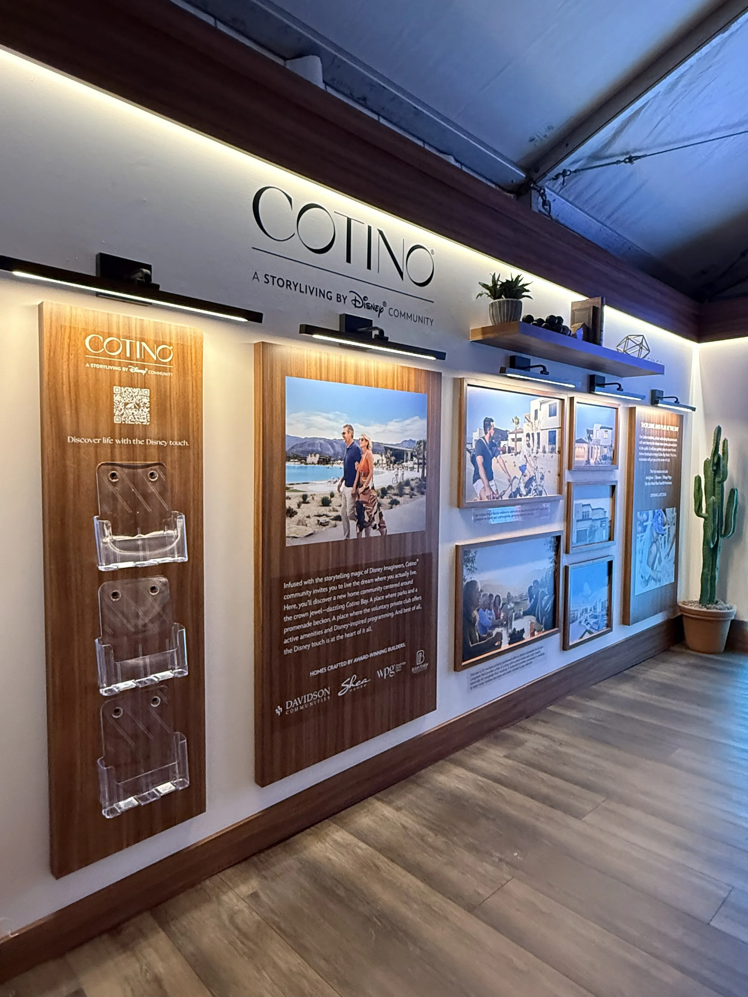 Display wall with promotional posters, framed images, and a potted cactus plant, featuring the branding 'COTINO' and information about a Disney community storytelling project.