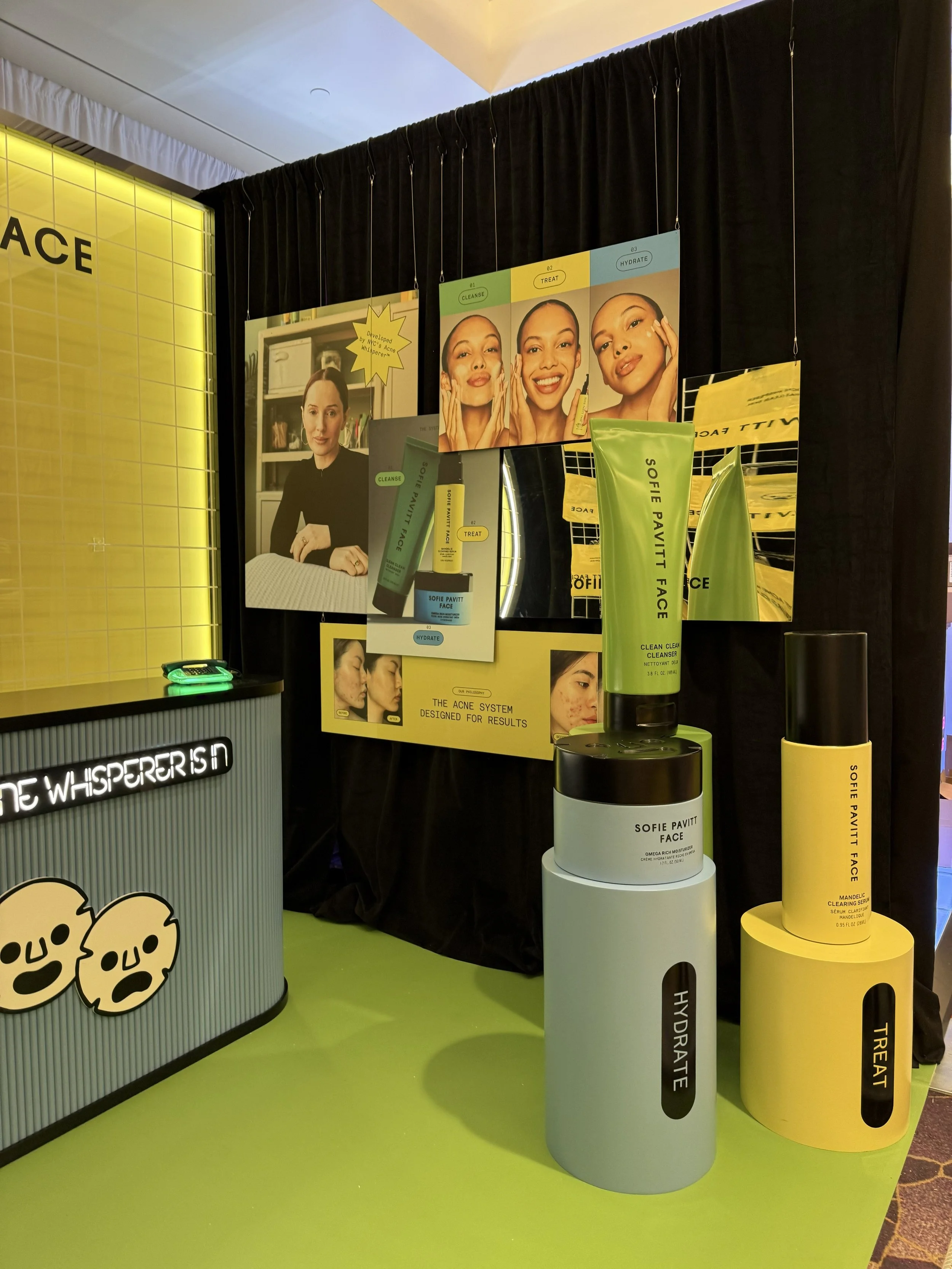 Display of skincare products by Sofie Pavitt Face, including moisturizer and serum, with posters illustrating the skincare routine steps: cleanse, treat, hydrate.