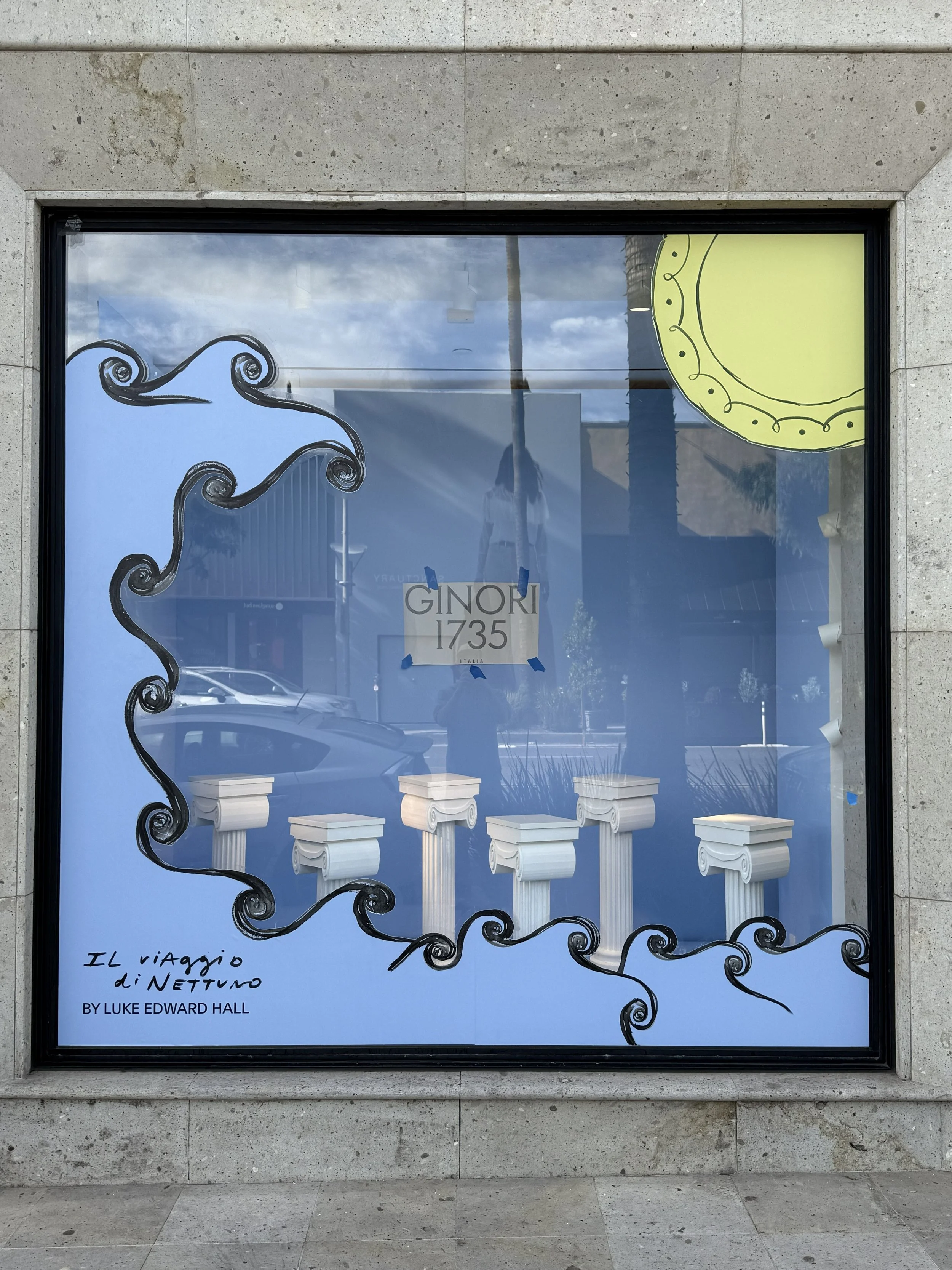 A window display features a drawing of four white classical columns and decorative black scrolls around the edges. A yellow half-circle shape is in the top right corner. The text in the bottom left corner says 'Il viaggio di Nettuno BY LUKE EDWARD HA