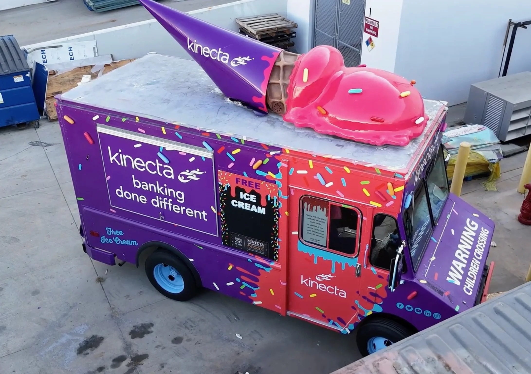 A replica ice cream truck decorated with colorful sprinkles, featuring the 'kinecta' logo and advertising free ice cream for children, with a large pink ice cream cone with sprinkles on top.