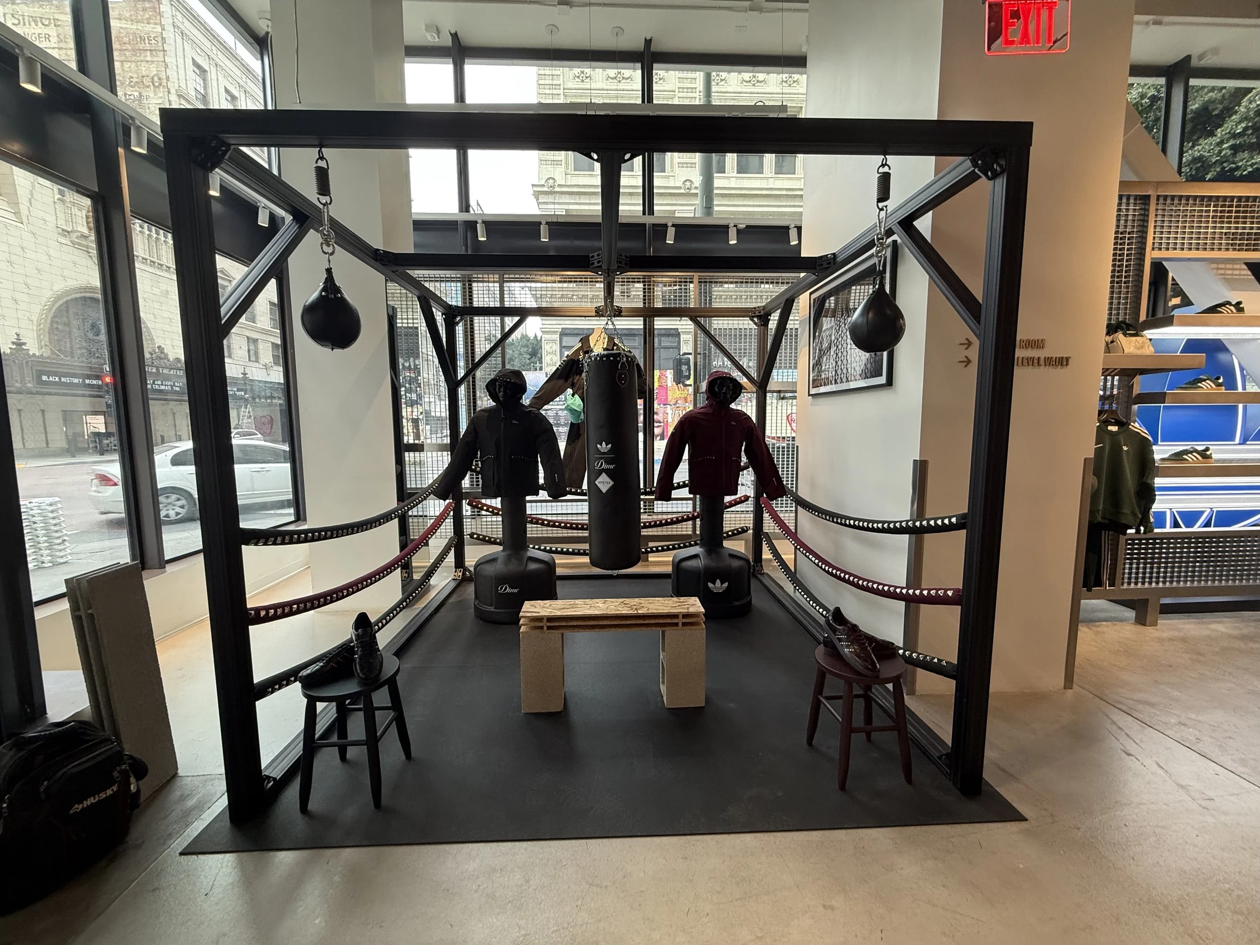 Inside a retail store featuring boxing equipment, mannequins dressed in sportswear, and shelves with athletic shoes, near large windows with a city view.