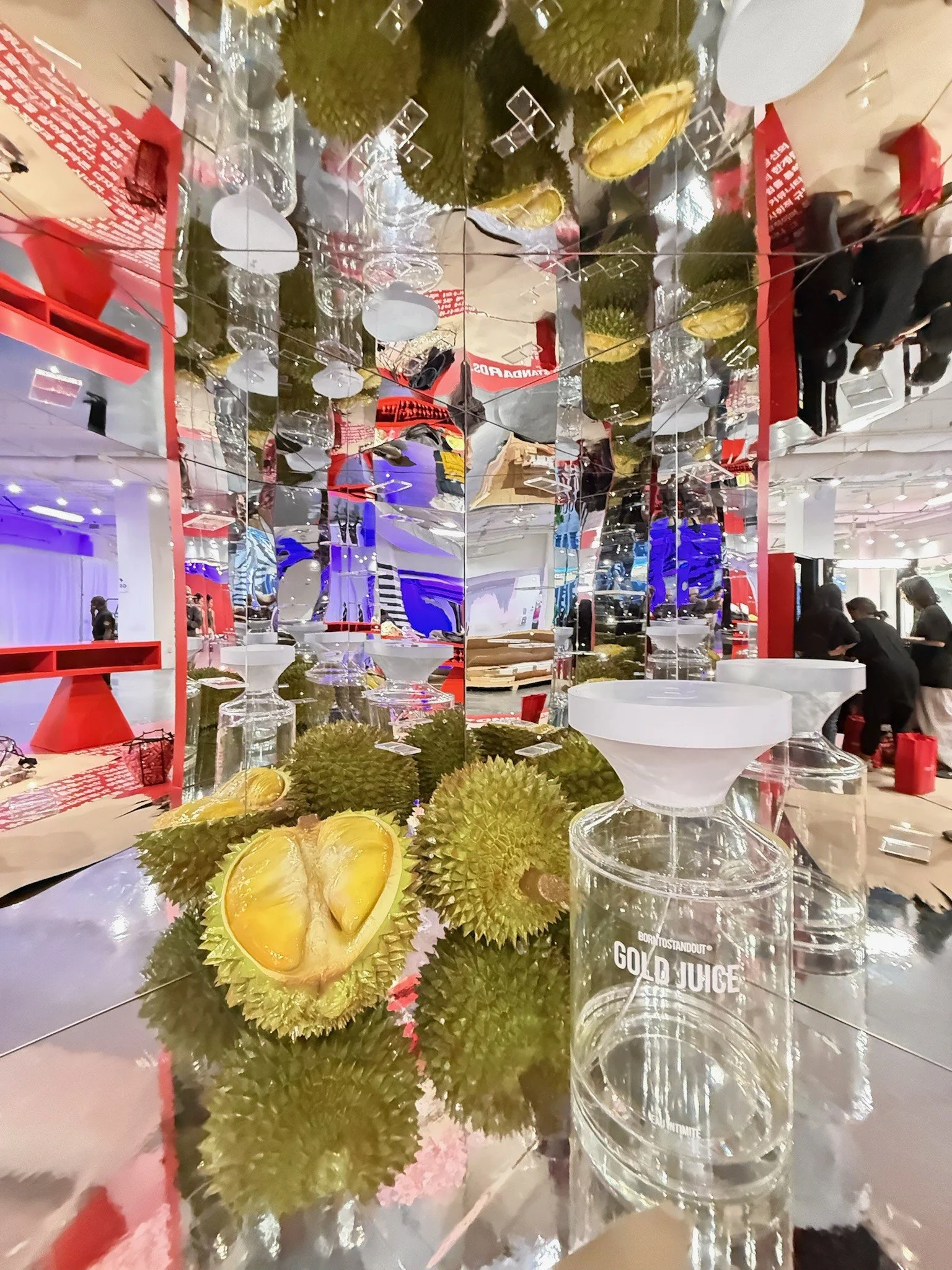 A table display with durian fruits and multiple clear glasses, some stacked, and a bottle of coconut juice in an indoor setting.