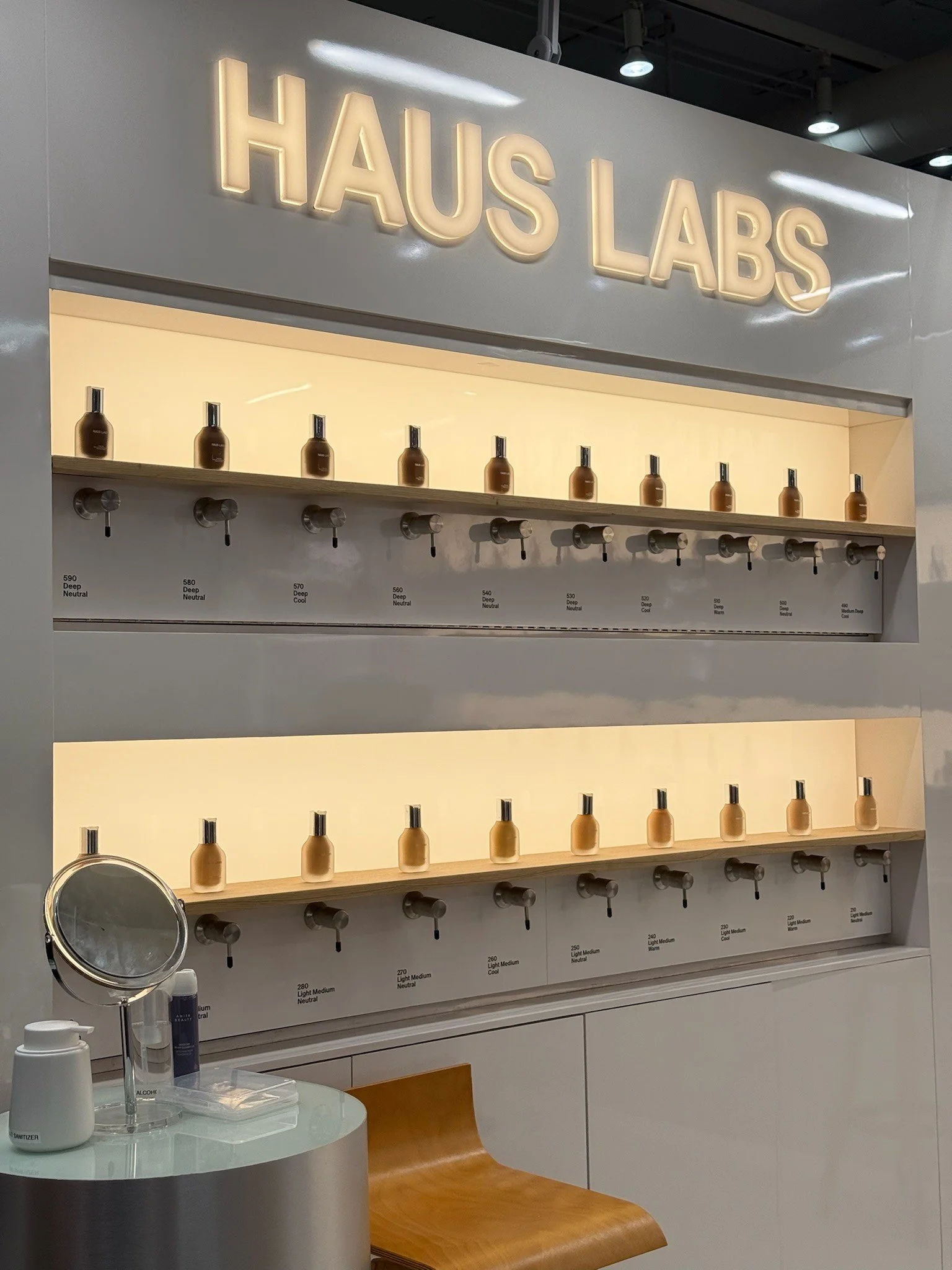 Display wall with various shades of beige and brown foundation bottles in a cosmetics store, with labeled swatches below.