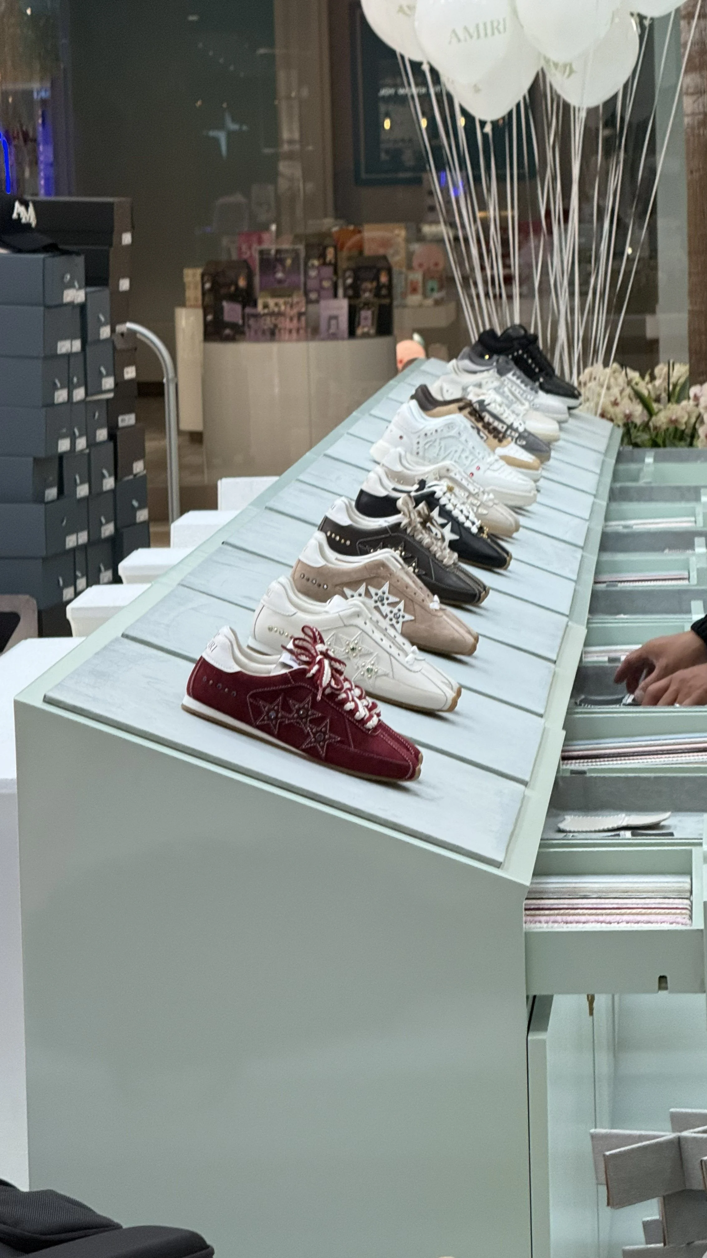 Display of various sneakers arranged on a white angled stand, with white balloons and store shelves in the background.
