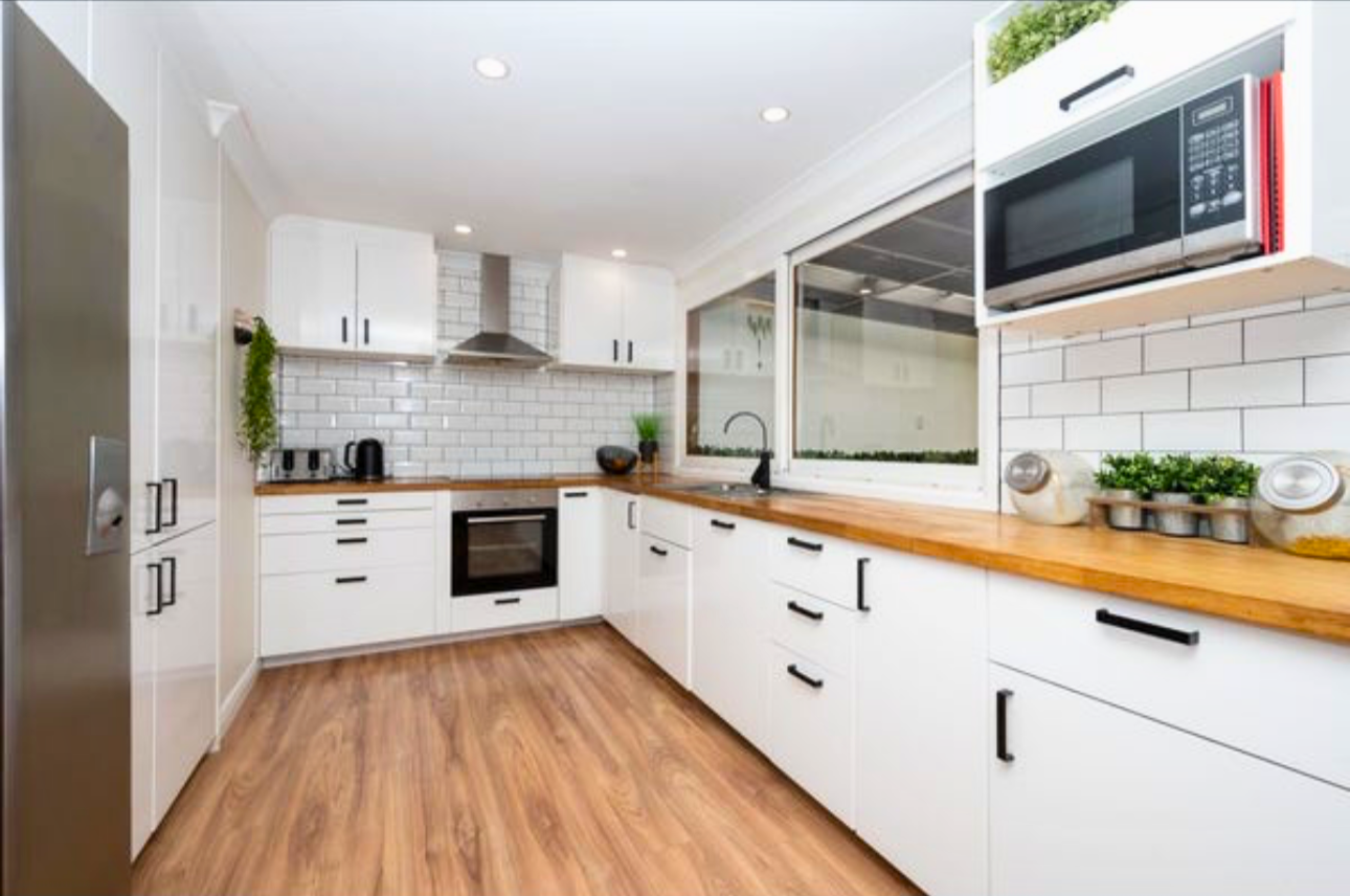 Modern kitchen with white cabinets, wood countertops, a stainless steel oven, microwave, and range hood, with a large window and hardwood floors.
