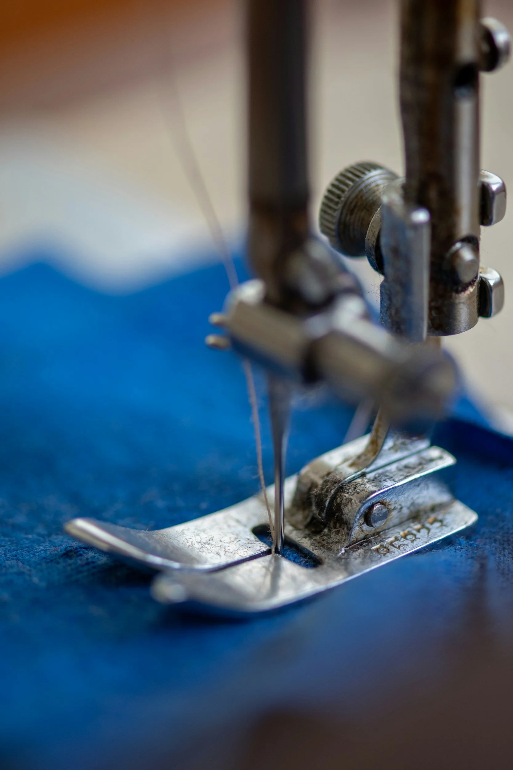 Close-up of a sewing machine needle sewing through blue fabric.