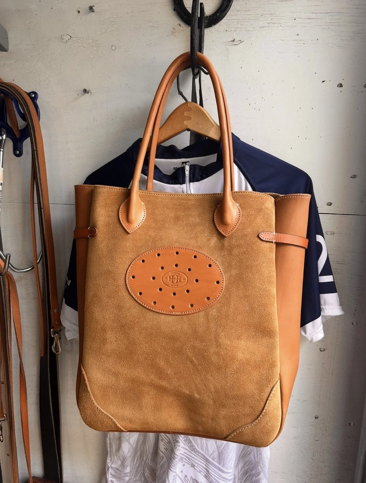 A large tan and orange tote bag hanging on a hook, with a navy and white sports jersey partially visible in the background.