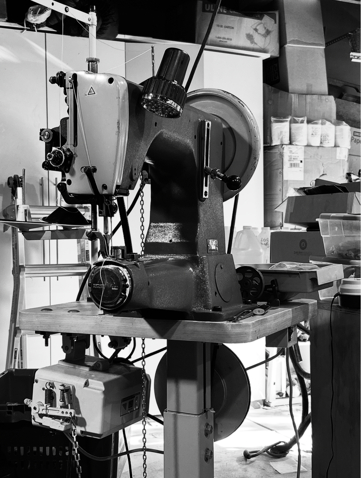 A vintage sewing machine on a wooden table in a workshop setting, surrounded by shelves and boxes.