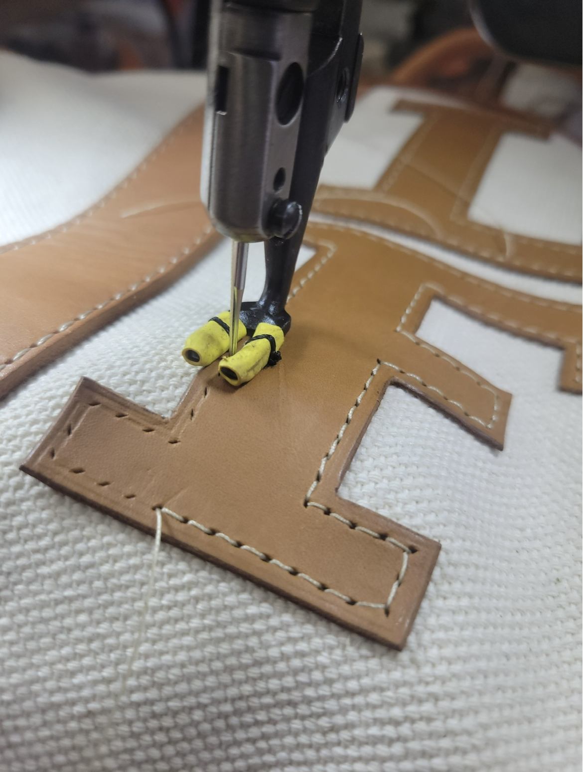 Close-up of a sewing machine stitching a large letter patch onto fabric, with yellow bobbins visible.