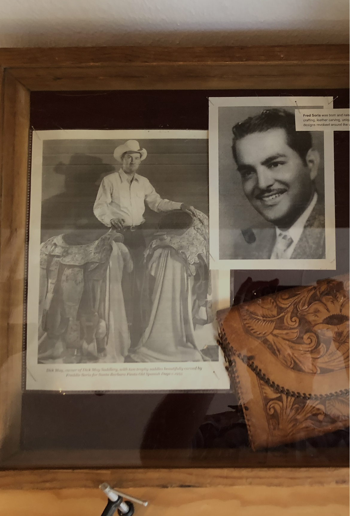 A display case with a black and white photograph of a man in a cowboy hat standing beside a decorated saddle, and a portrait photograph of a smiling man with dark hair.
