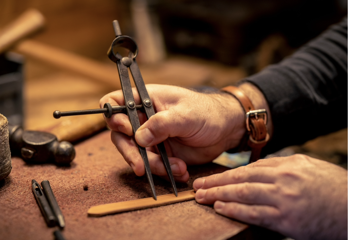 A craftsman is using a divider to mark a line on a piece of wood in a woodworking shop.