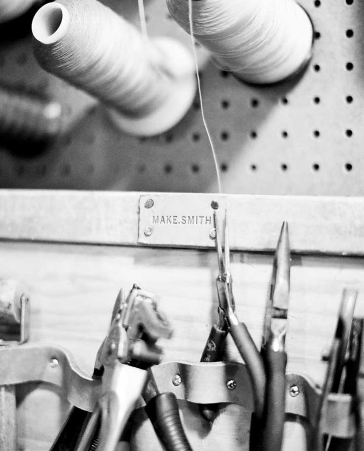 Close-up of sewing tools including scissors, pins, and spools of thread mounted on a pegboard with a label reading 'MAKE.SMITH'.