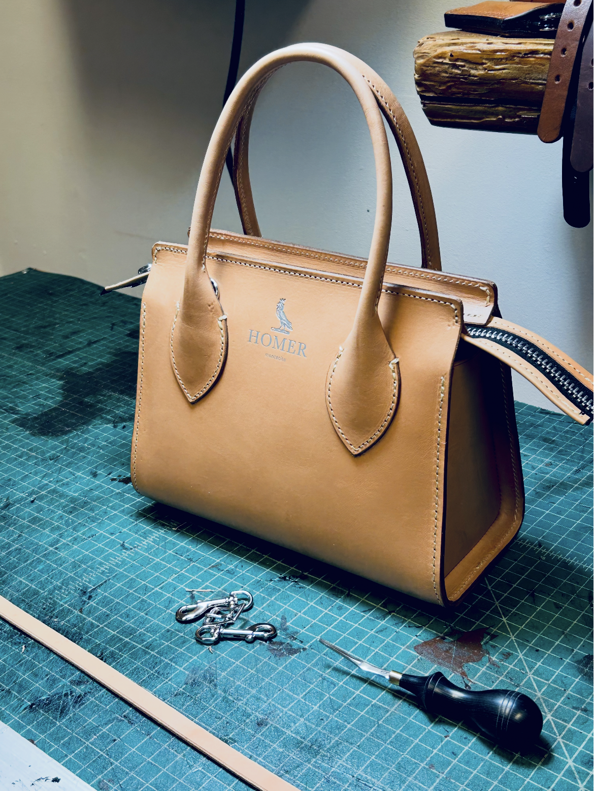 Leather handbag with brand logo on a worktable with tools and hardware.