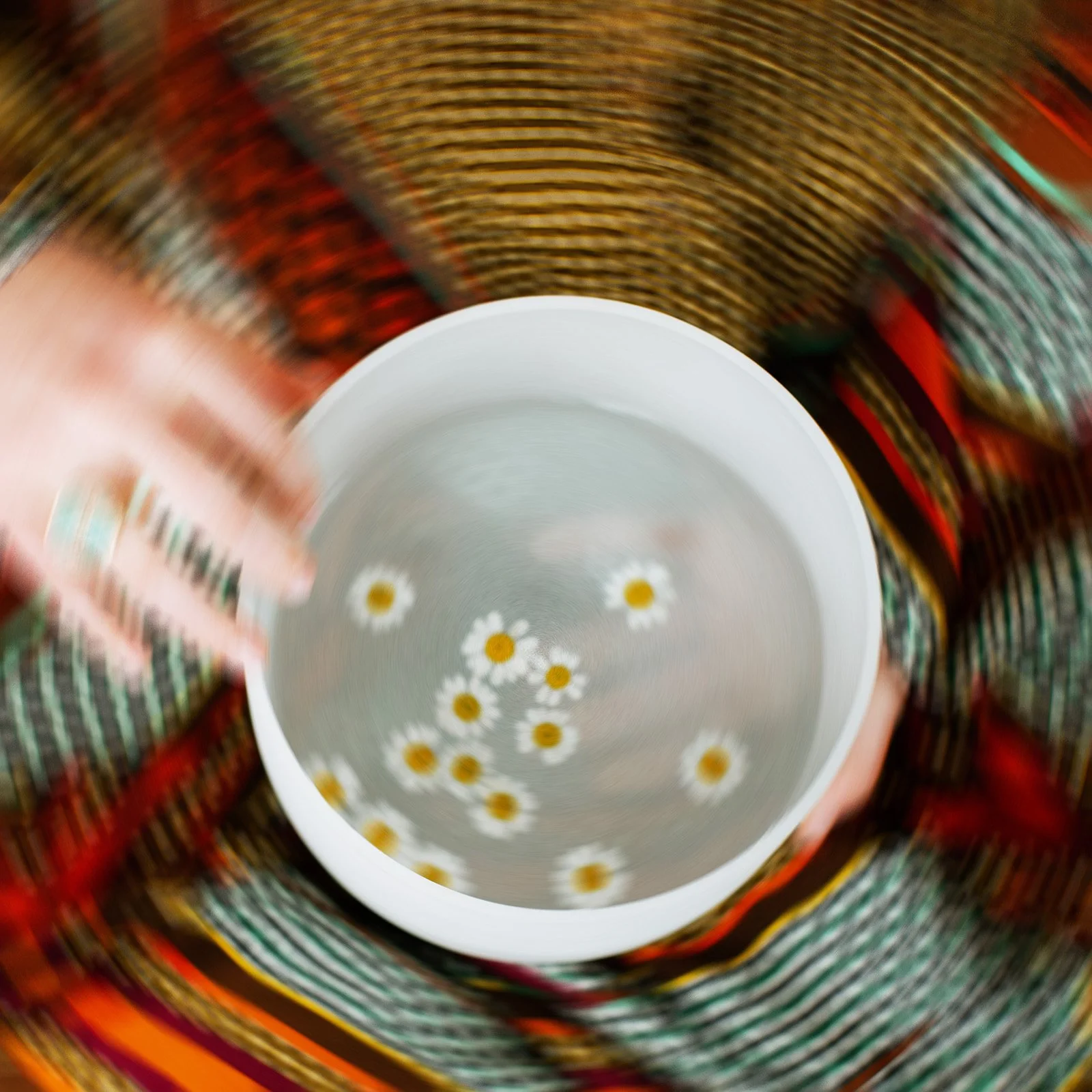 motion blurred photo of Laura holding singing bowl in her lap (aerial view) with chamomile floating in circles