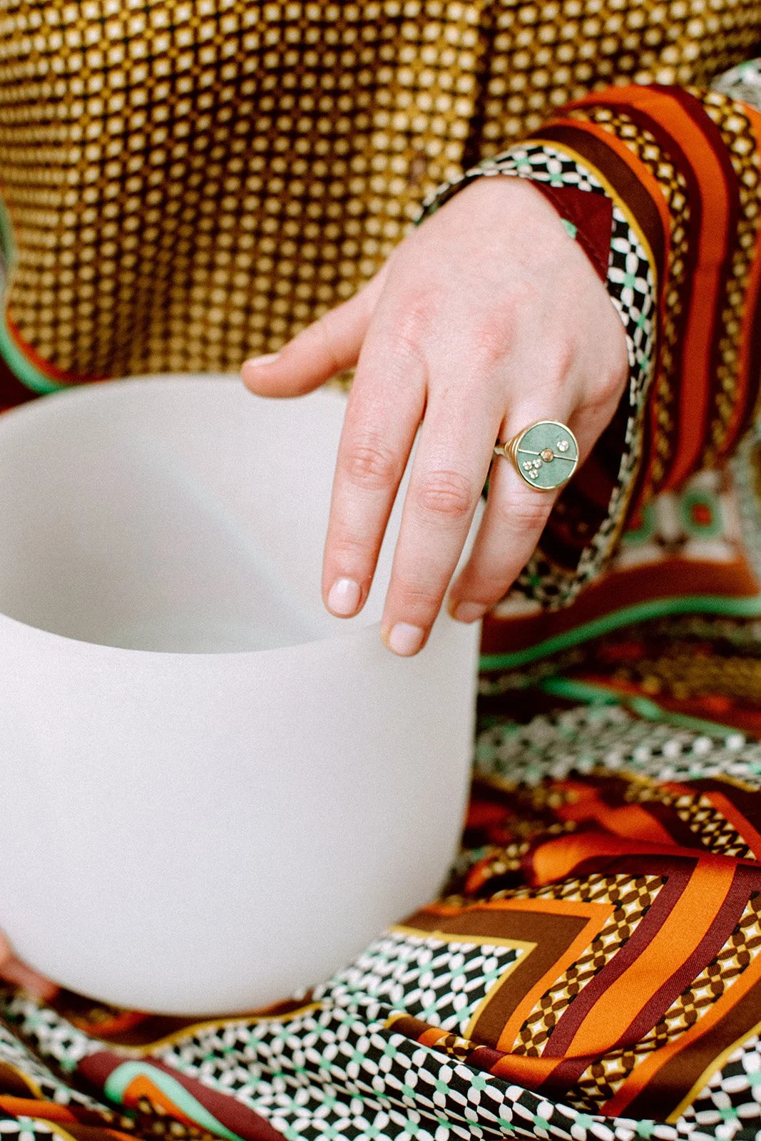 Woman's hand with a turquoise ring holding a singing bowl in her lap in a patterned outfit