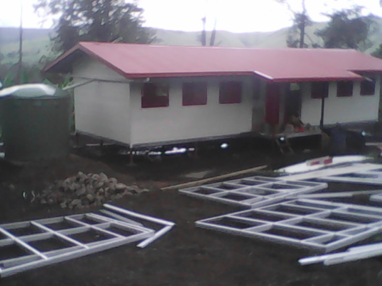 A house under construction with metal framing on the ground in front of it.