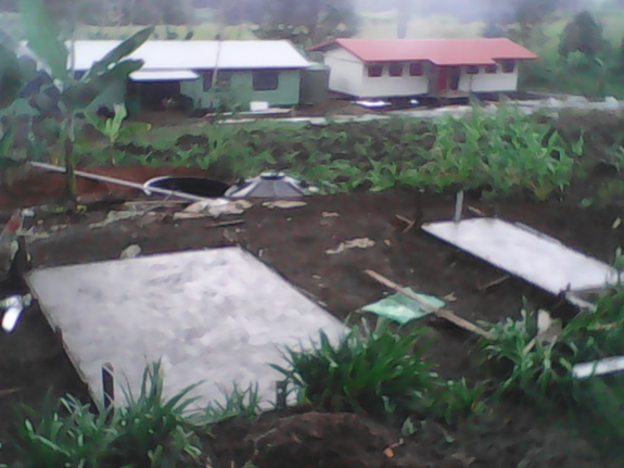 Construction site with concrete slabs and construction tools in a rural area with houses and green vegetation in the background.