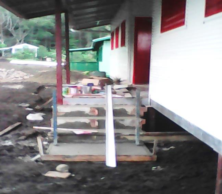Front porch of a house with red window frames, stairs with a handrail, and construction supplies on the porch.
