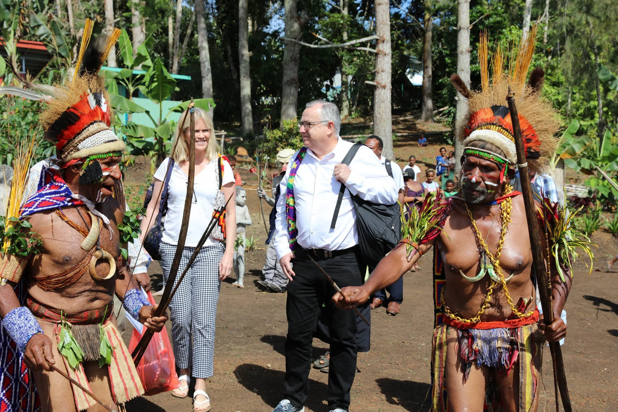Group of indigenous men in traditional attire and western visitors talking in a forest clearing.