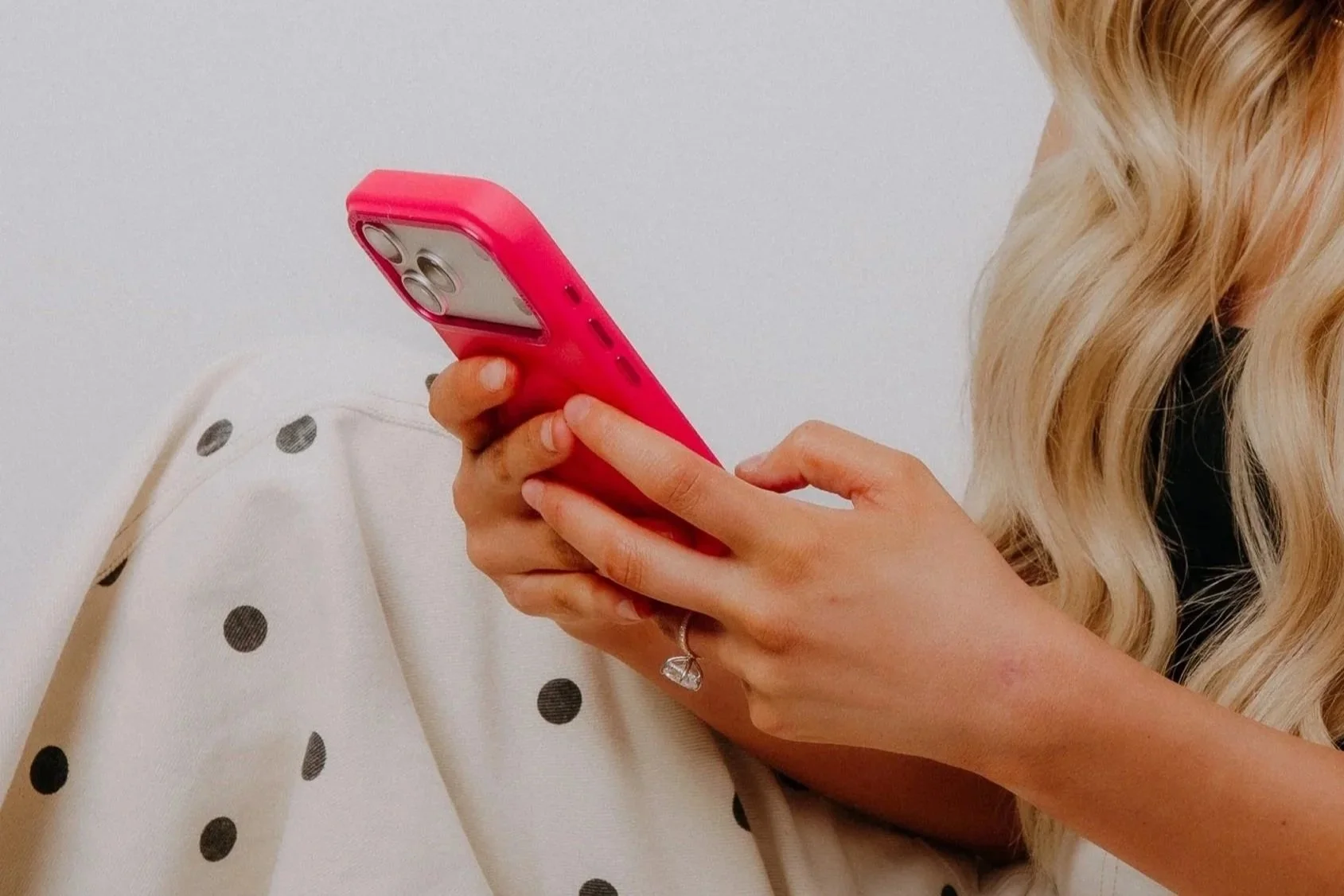 A woman with blonde hair holding a pink smartphone.