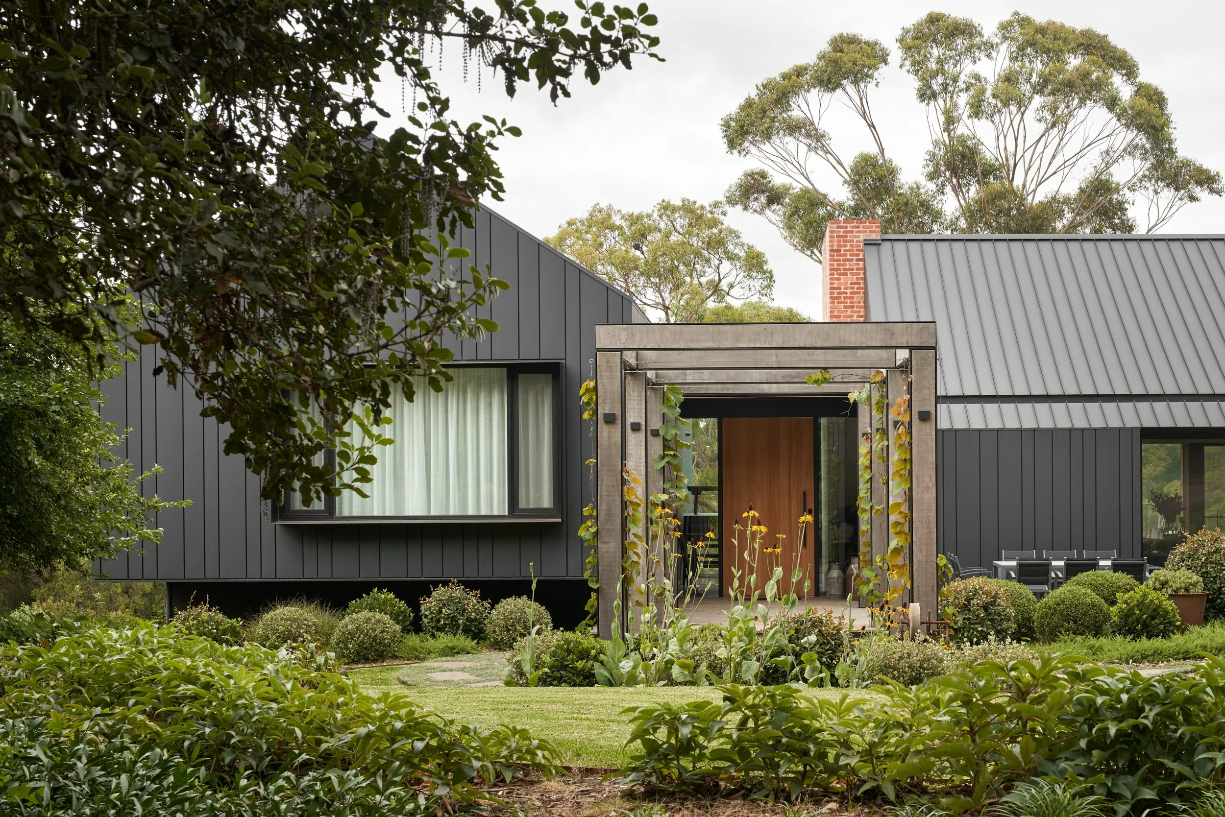 Modern house with black vertical siding and metal roof, surrounded by lush greenery and a landscaped garden