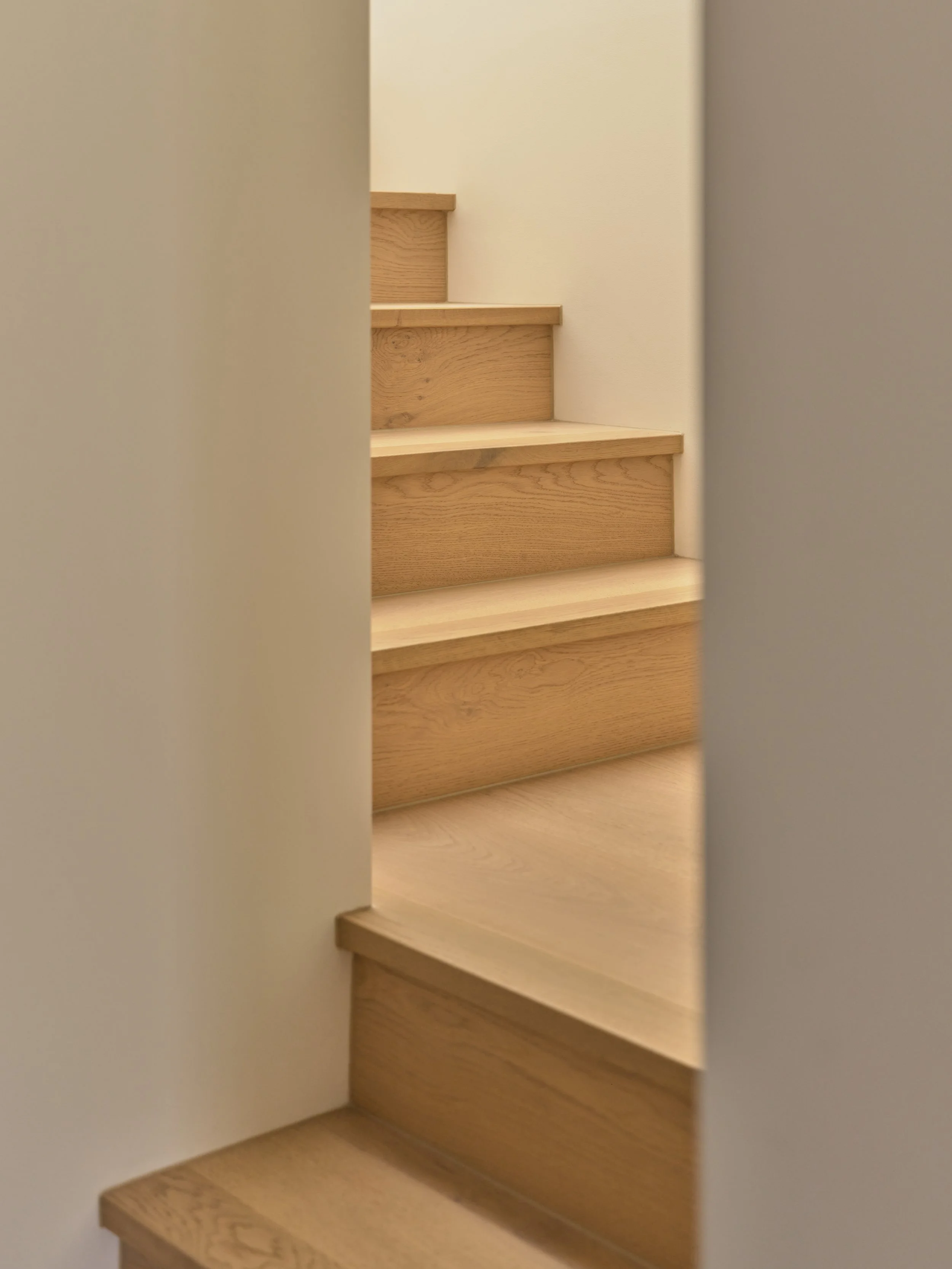 Wooden staircase viewed through a narrow gap between two walls.