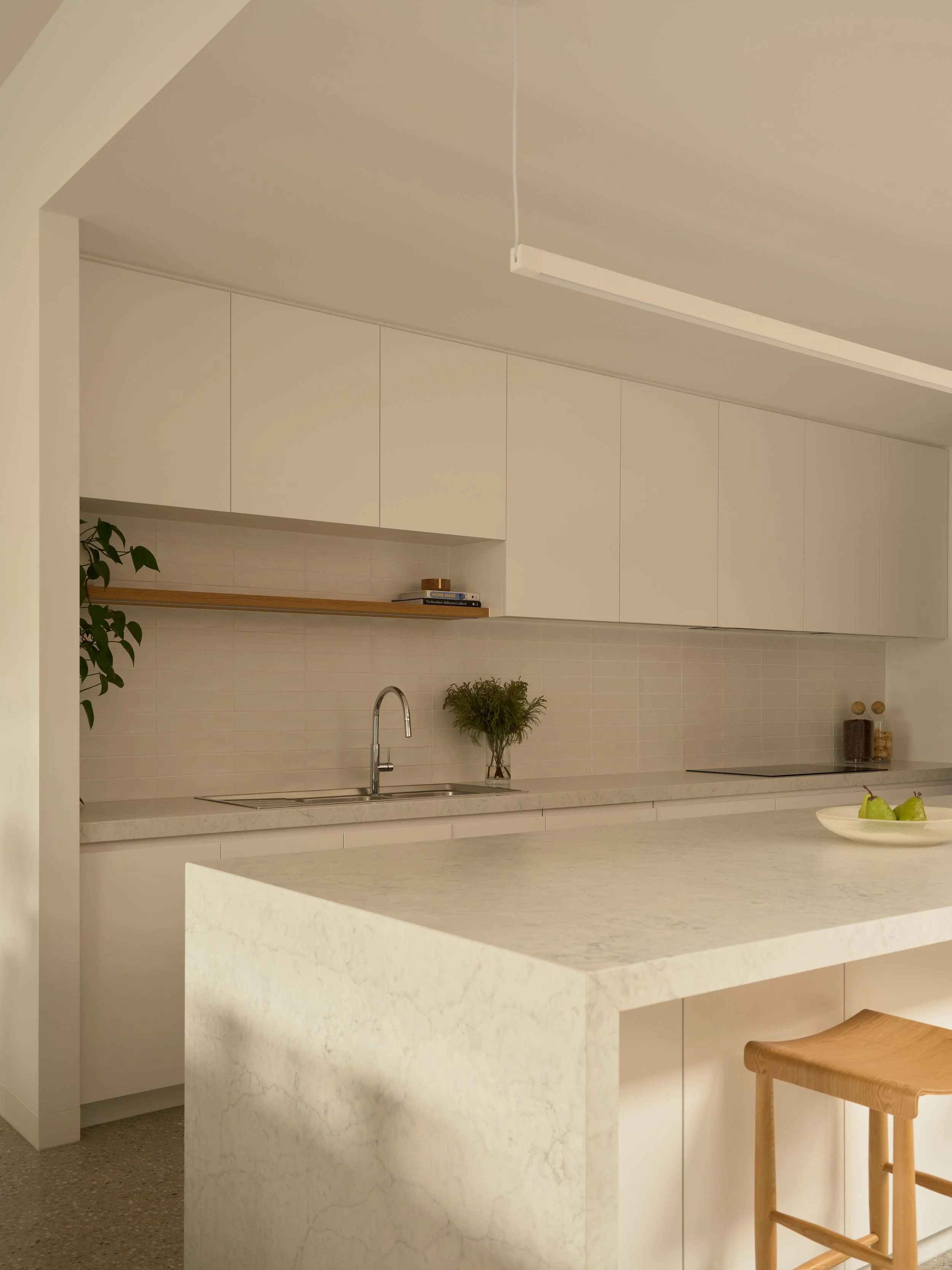 Modern minimalist kitchen with white cabinets, marble countertop, and a small wooden stool.