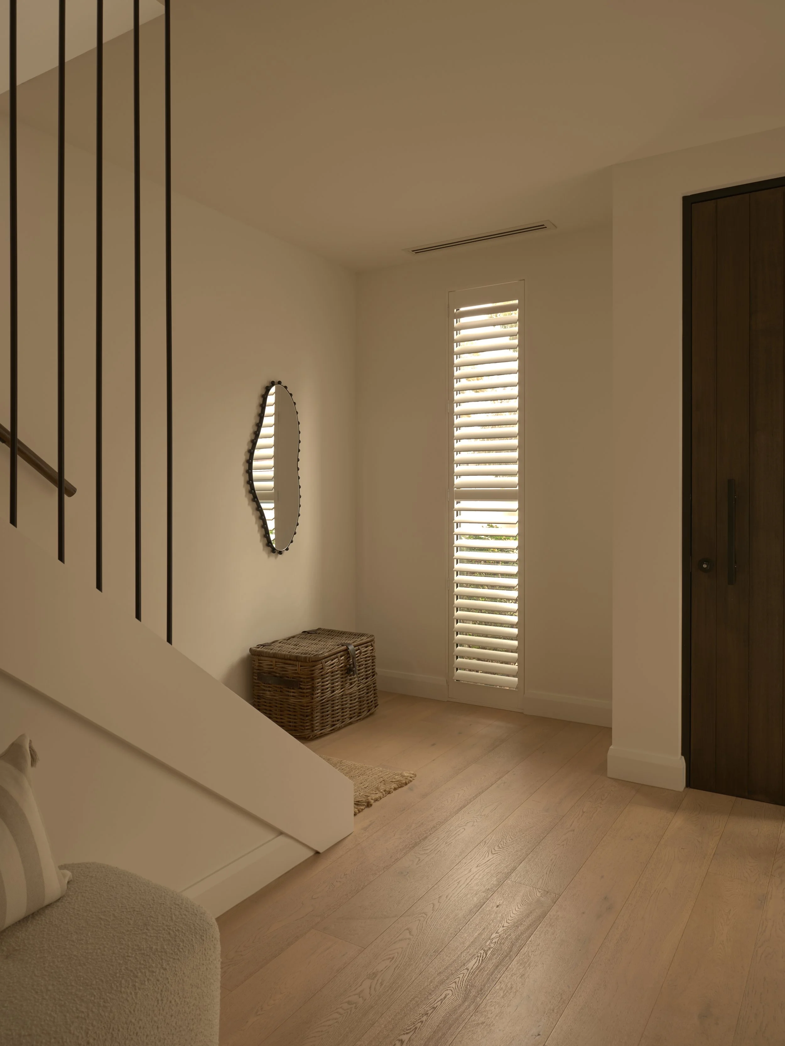 Bright entryway with wooden flooring, a wicker basket, a small mirror, and window shutters.