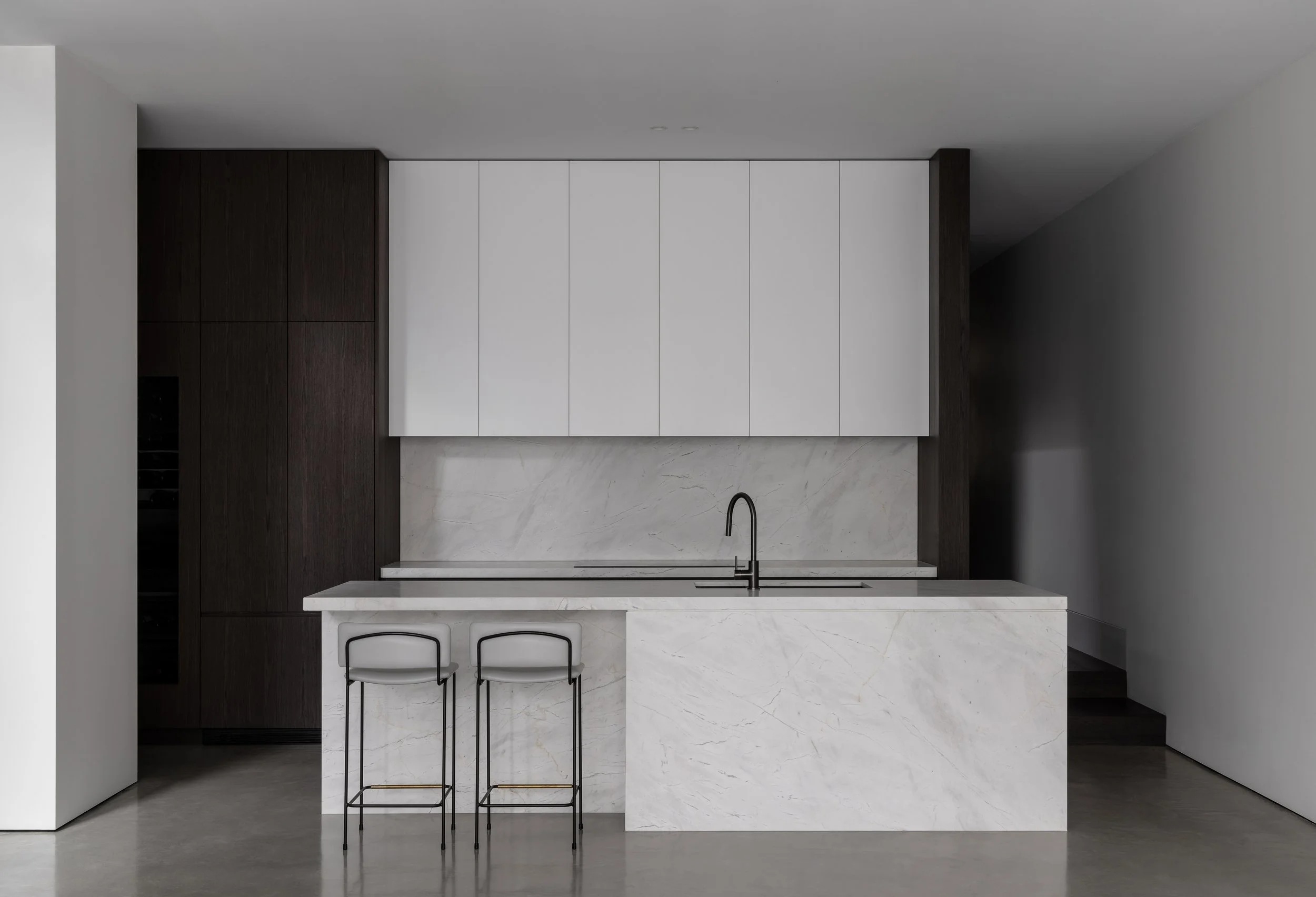 Modern kitchen with white marble island, black faucet, white upper cabinets, dark wood lower cabinets, and two bar stools.