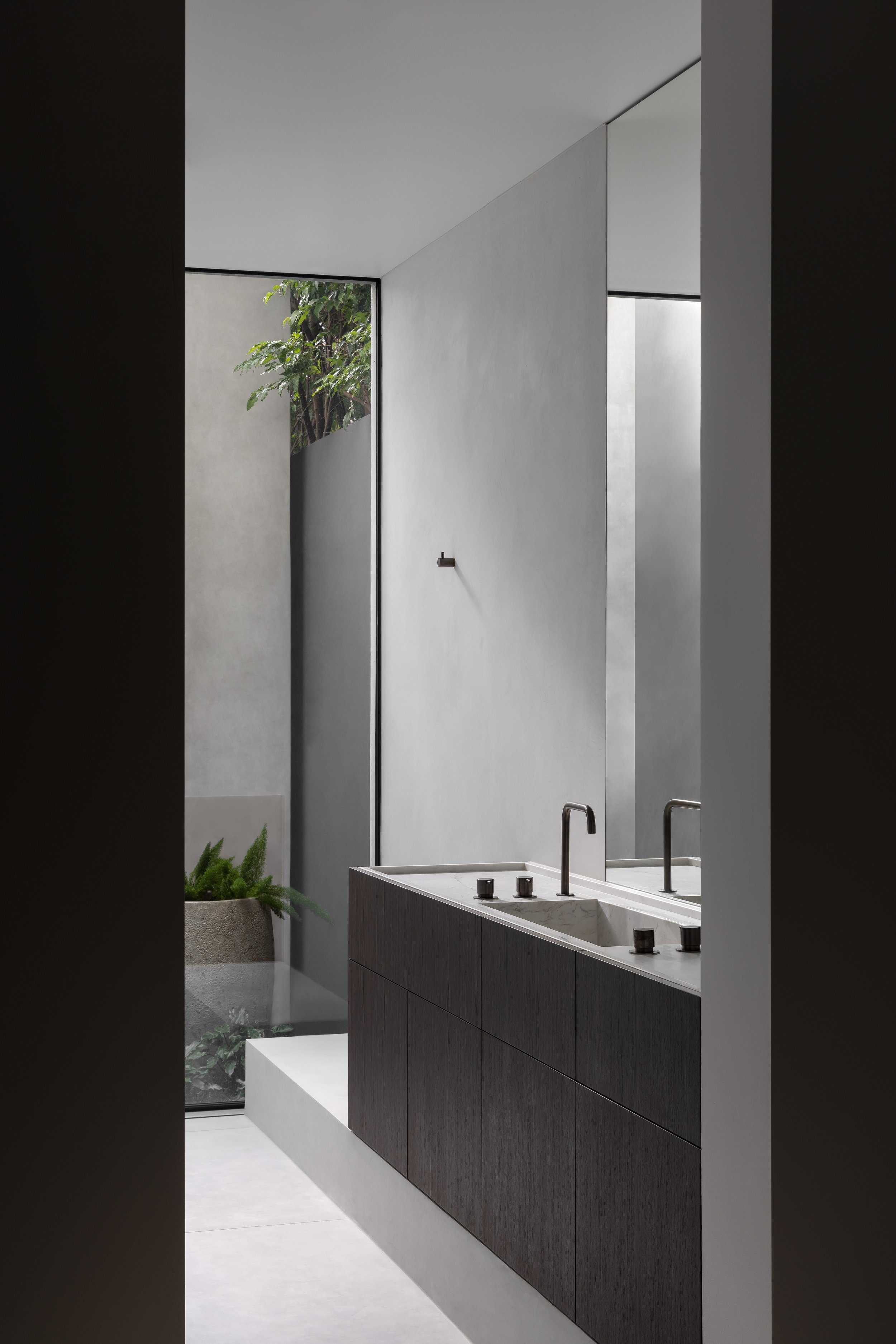 Modern bathroom with dark wooden vanity, marble sink, black faucets, large mirror, gray walls, and a window revealing greenery outside.