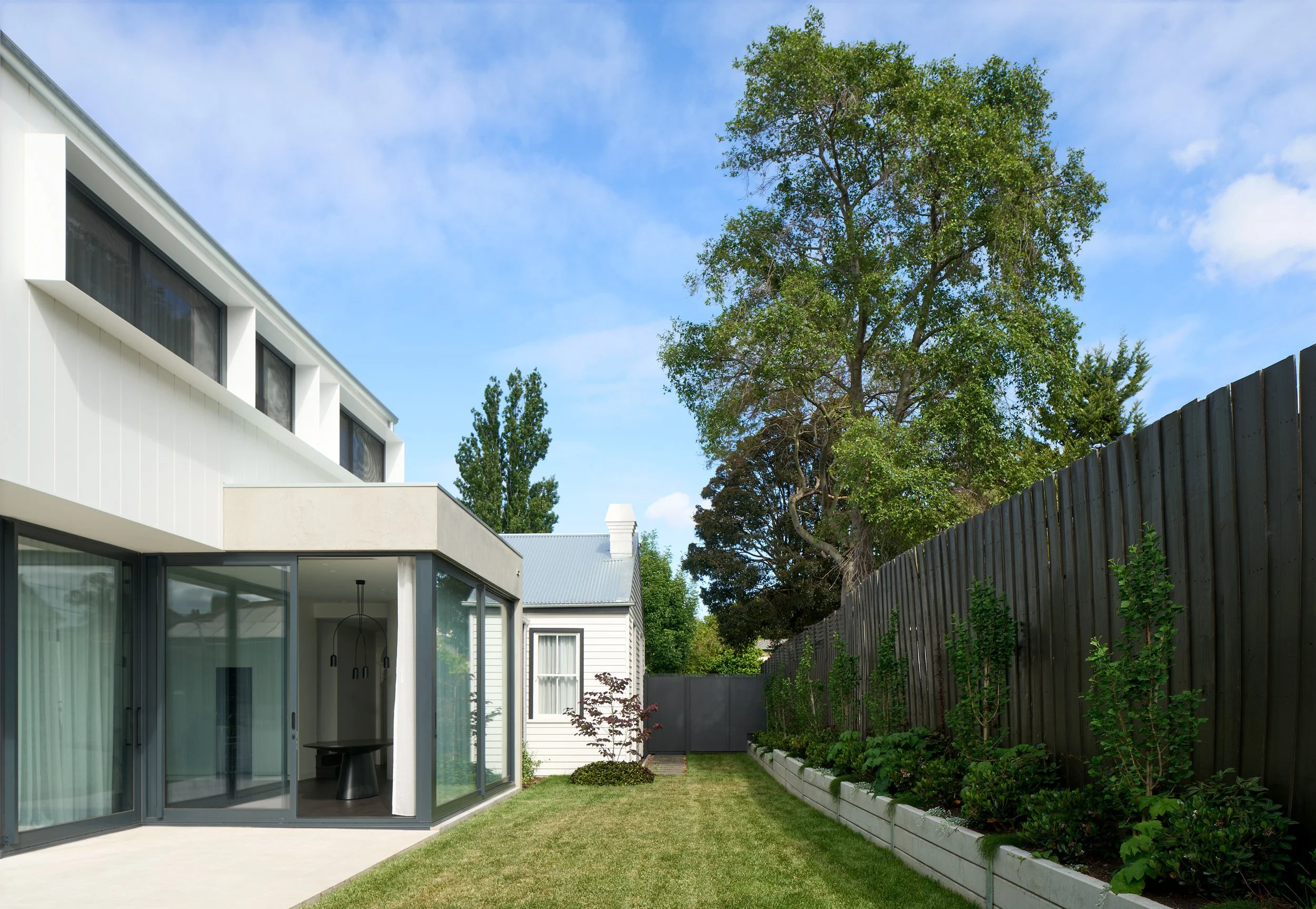 A modern house with large glass windows and a small backyard garden with a wooden fence and trees.