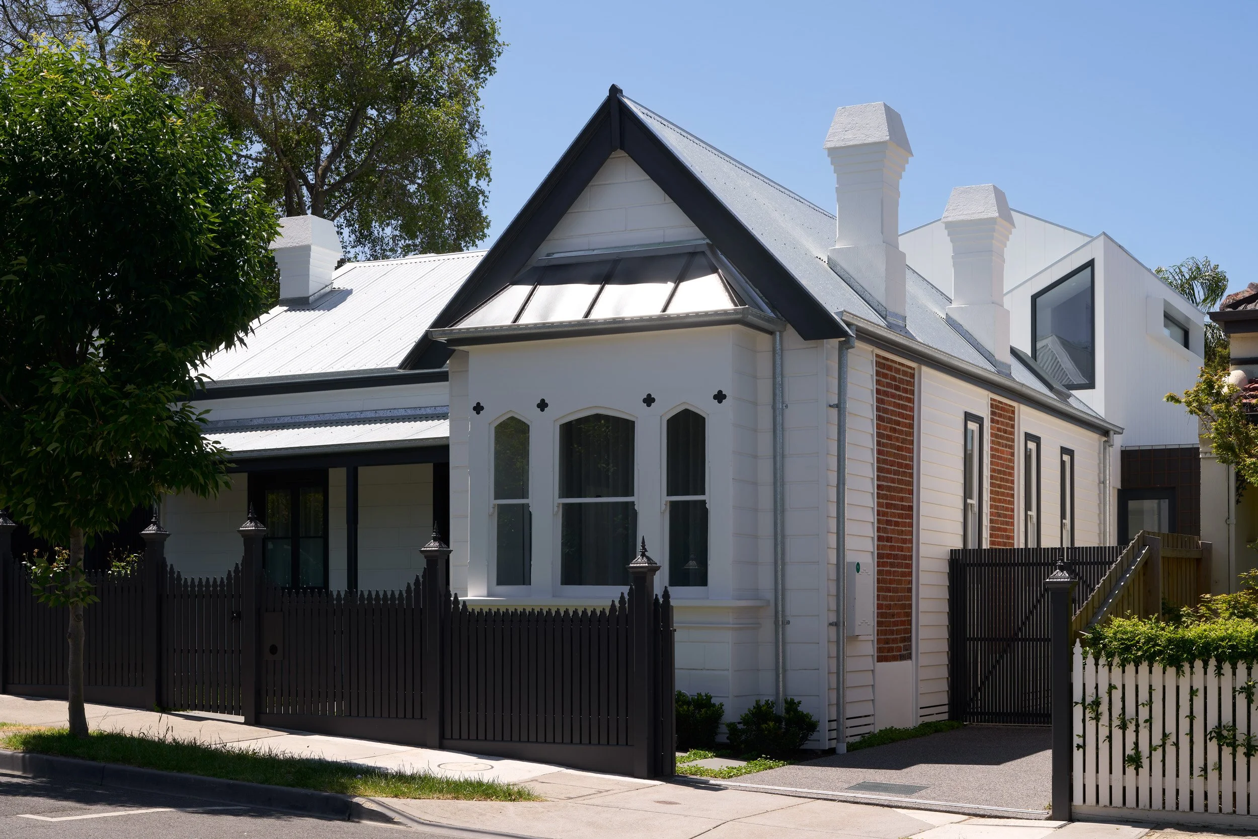 A modern house with white walls, a gabled roof, and a fenced yard, surrounded by trees.