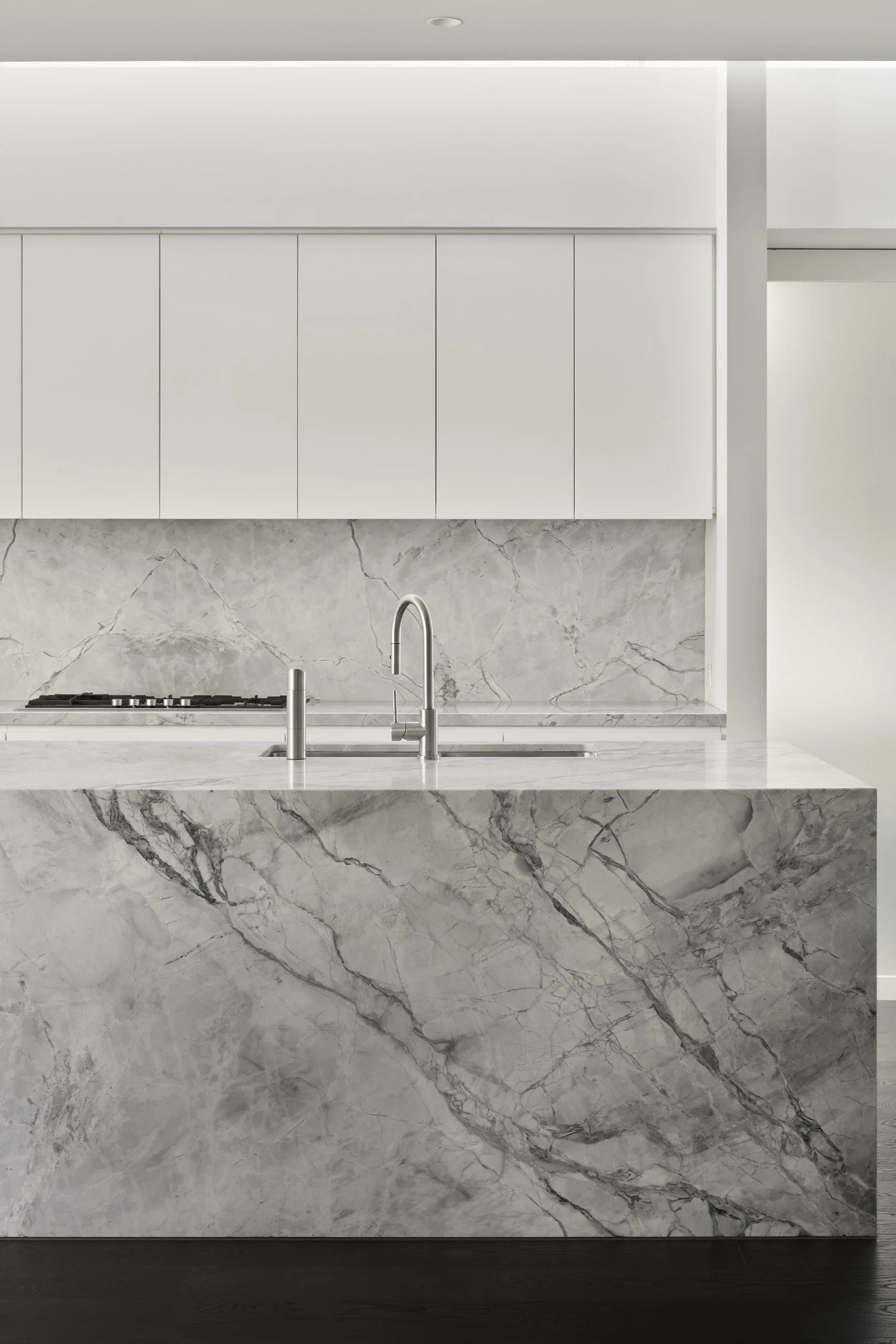 Modern kitchen with white cabinets, marble countertop, and marble backsplash, stainless steel faucet.