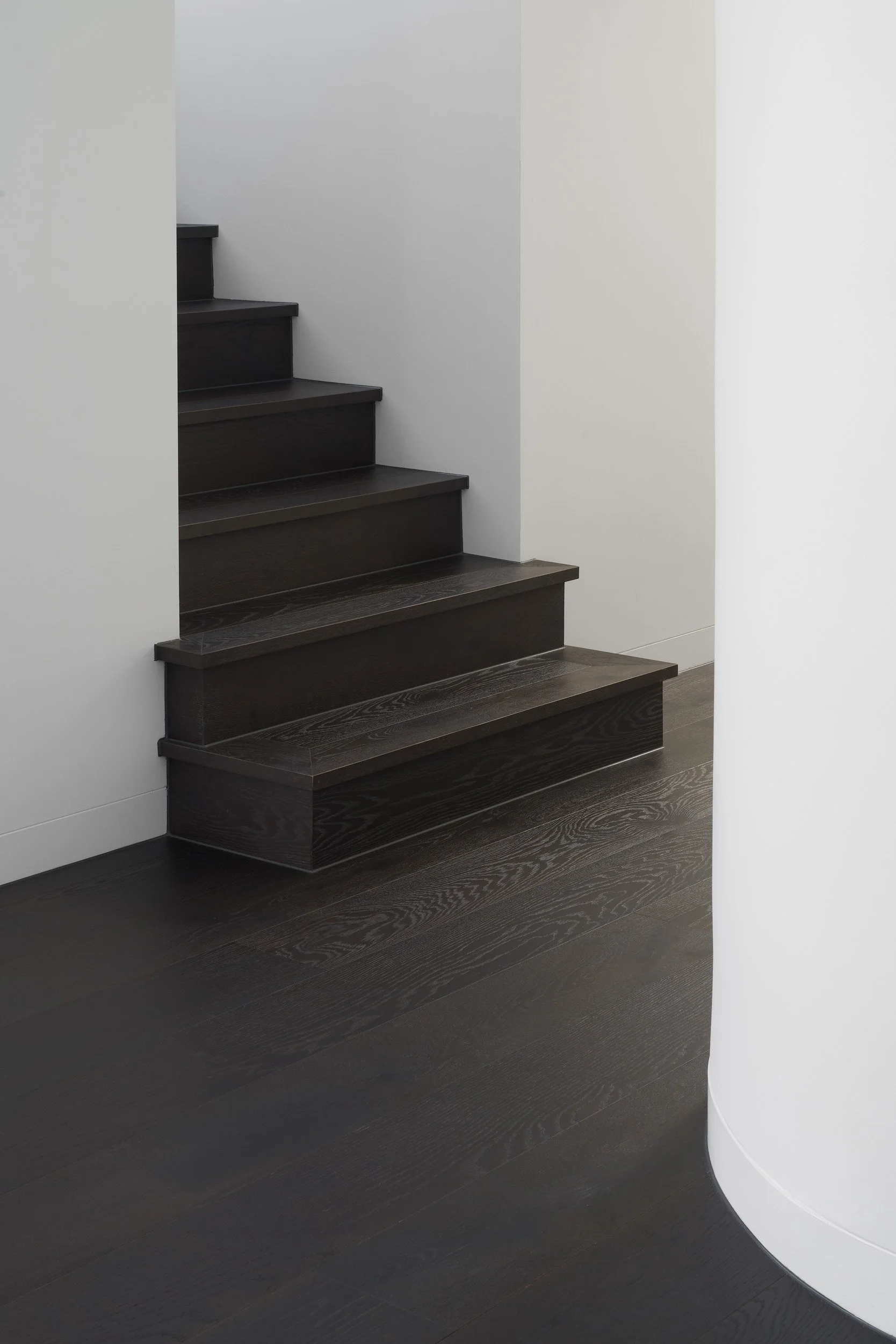 Dark wooden staircase with a wall on each side, in a minimalistic modern interior.