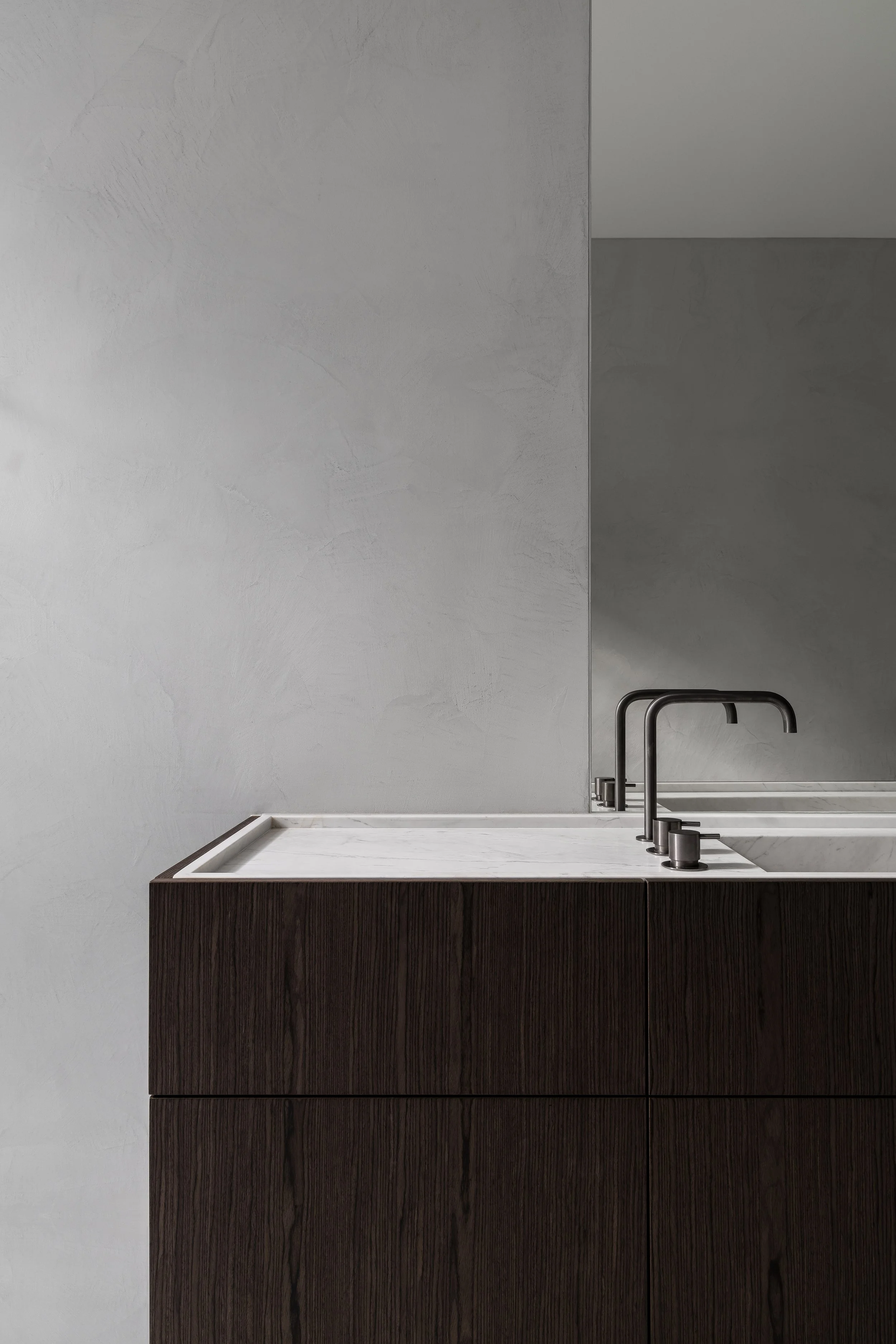 A modern bathroom sink with a dark wood vanity, white marble countertop, and black faucets against a textured light gray wall.