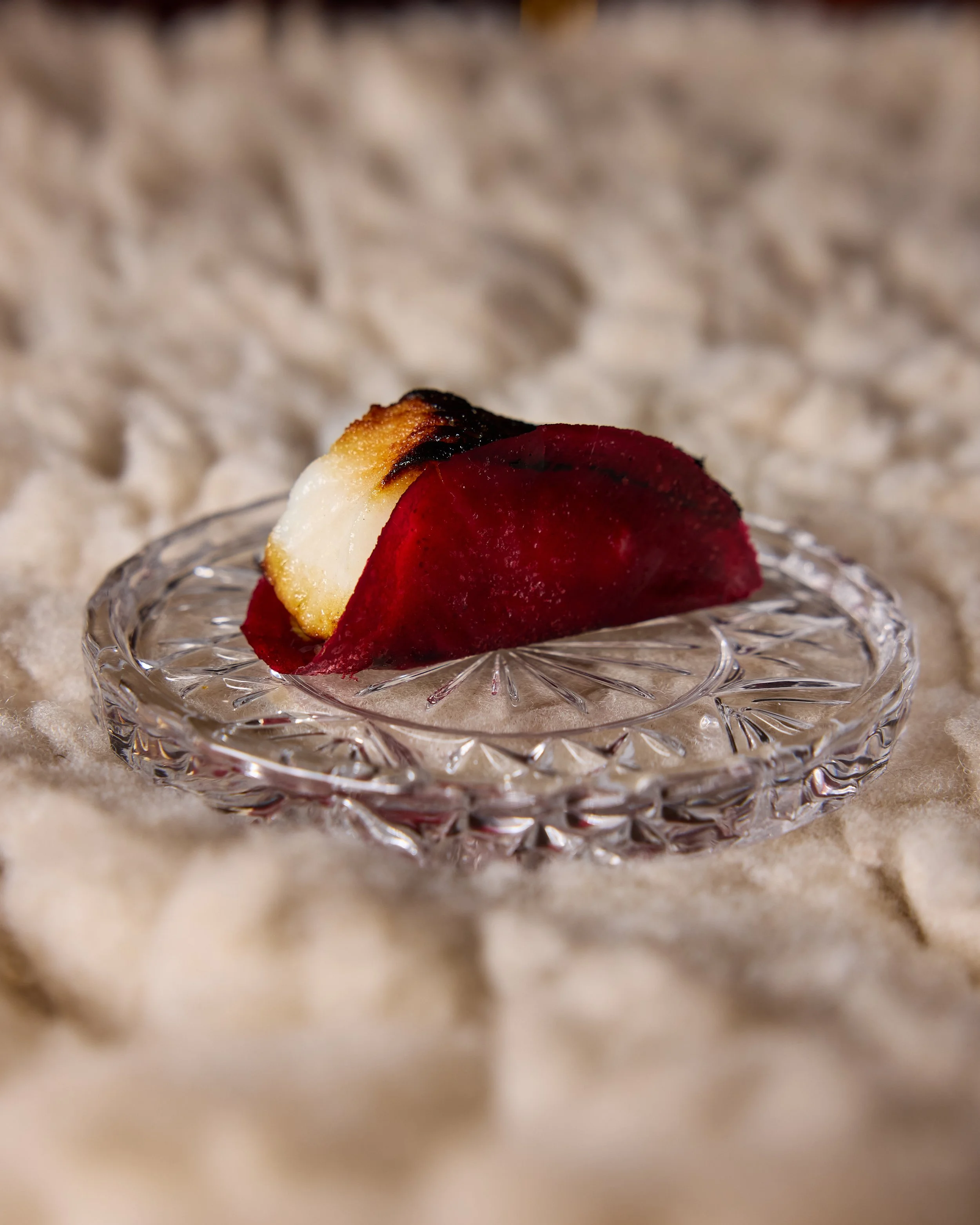 Close-up of a slice of pastry on a decorative glass plate, with a blurred, textured surface in the background, example of a dish at The Lore.