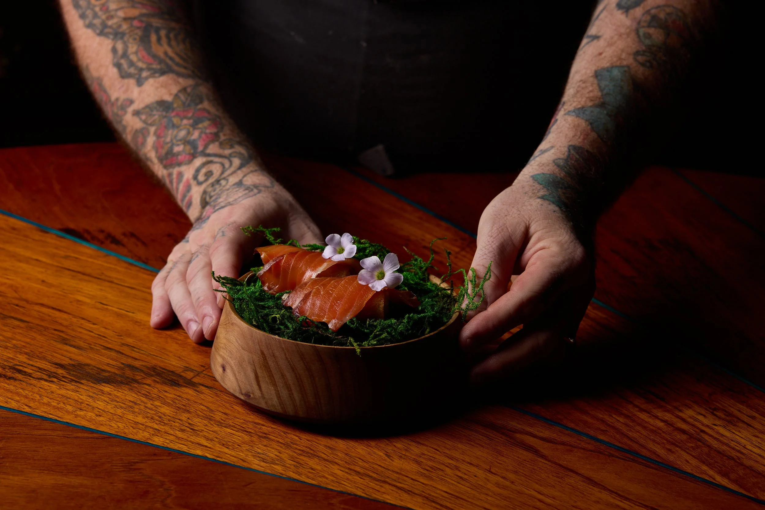 Hands placing a bowl of sushi on a wooden table, example of a dish at The Lore.
