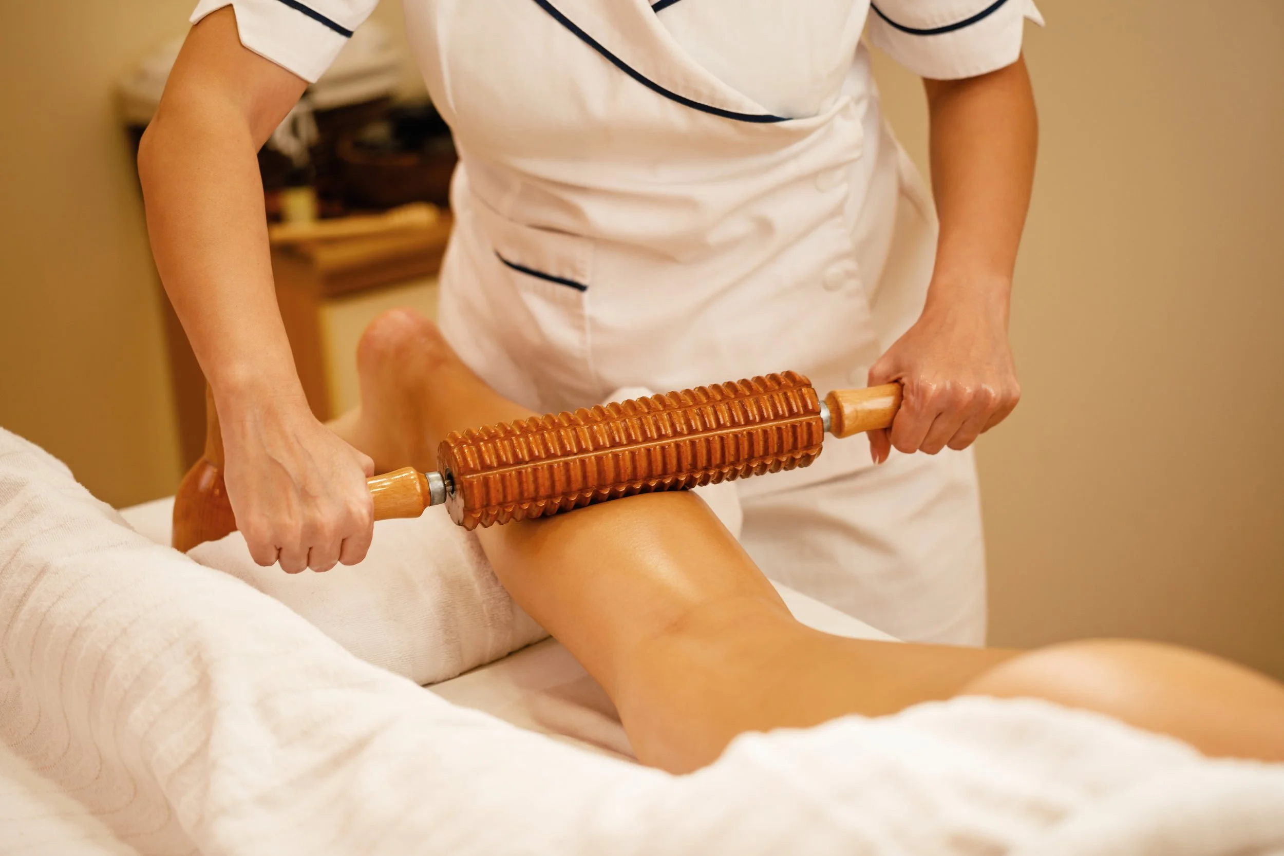 A massage therapist is using a wooden roller on a client's thigh during a massage.