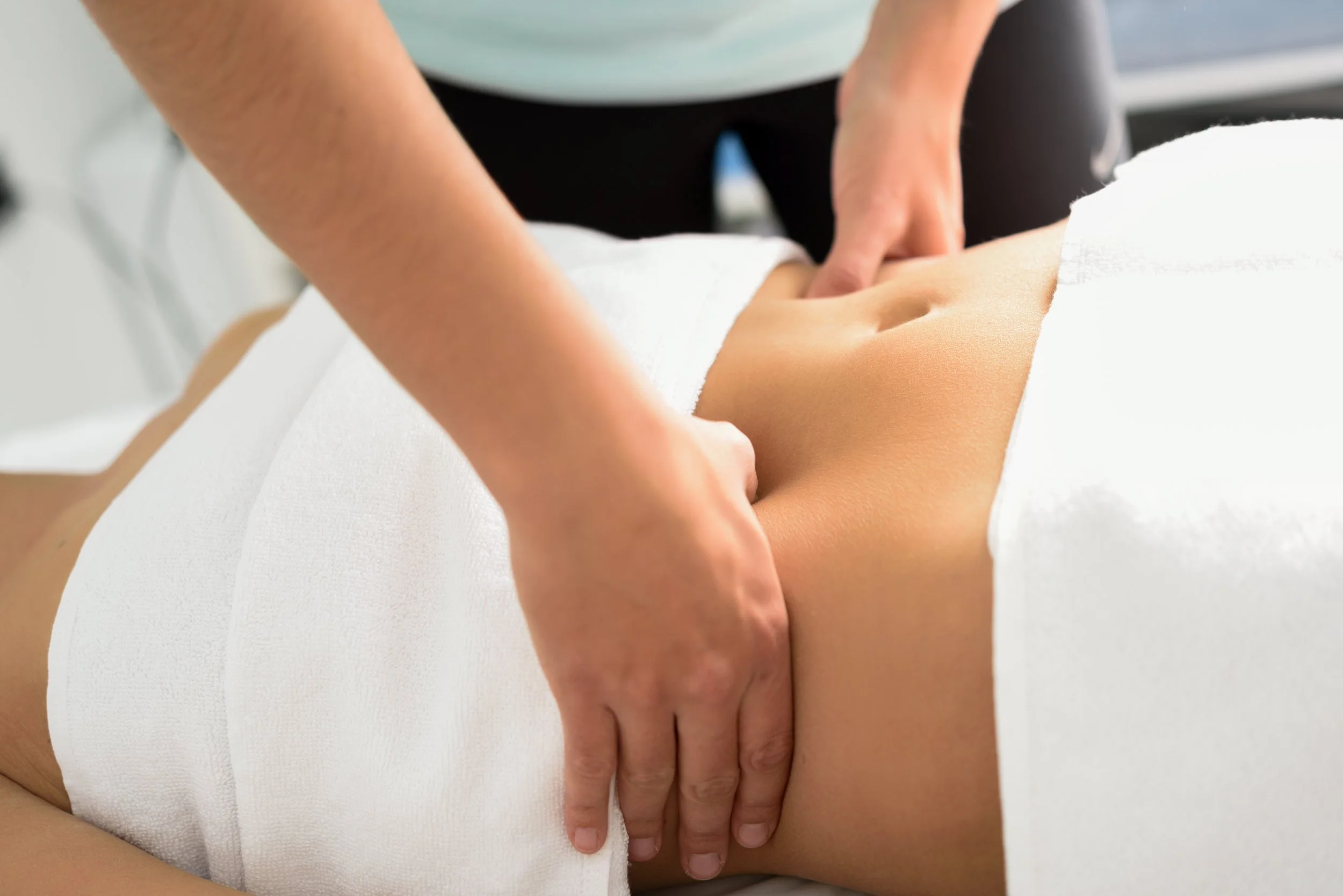 A person lying face down on a massage table getting a massage on their abdomen from a massage therapist.