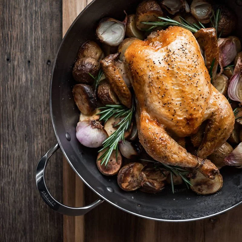 Roast chicken with herbs, garlic, and roasted potatoes in a skillet.