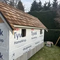 Side of a house under construction with Tyvek HomeWrap installed and a shingled roof.
