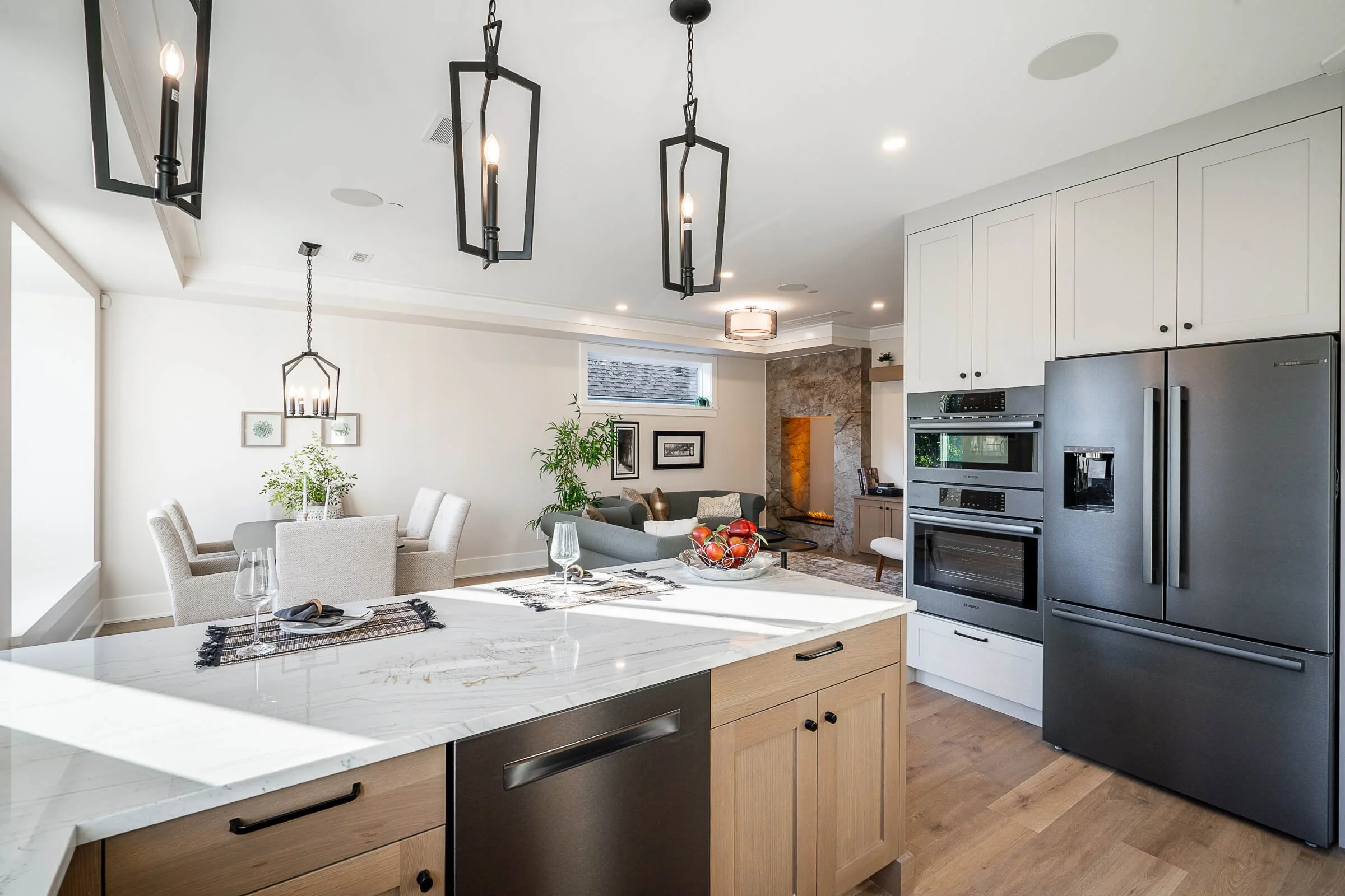 Modern open-concept kitchen and living room with white cabinets, stainless steel appliances, wooden flooring, and a fireplace with seating area.