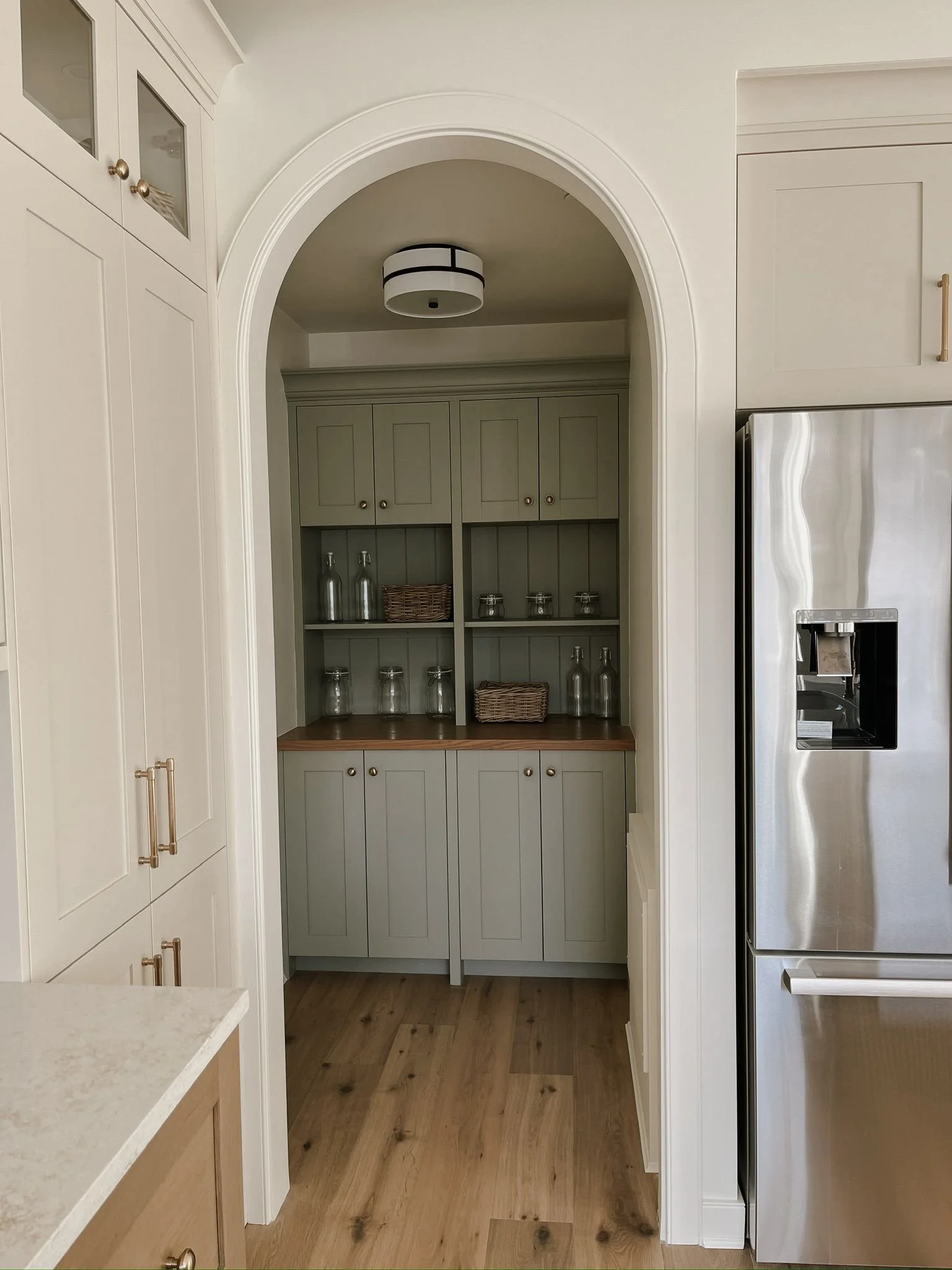 Kitchen with built-in shelves, cabinets, a wooden countertop, glass jars, bottles, baskets, and a stainless steel refrigerator.