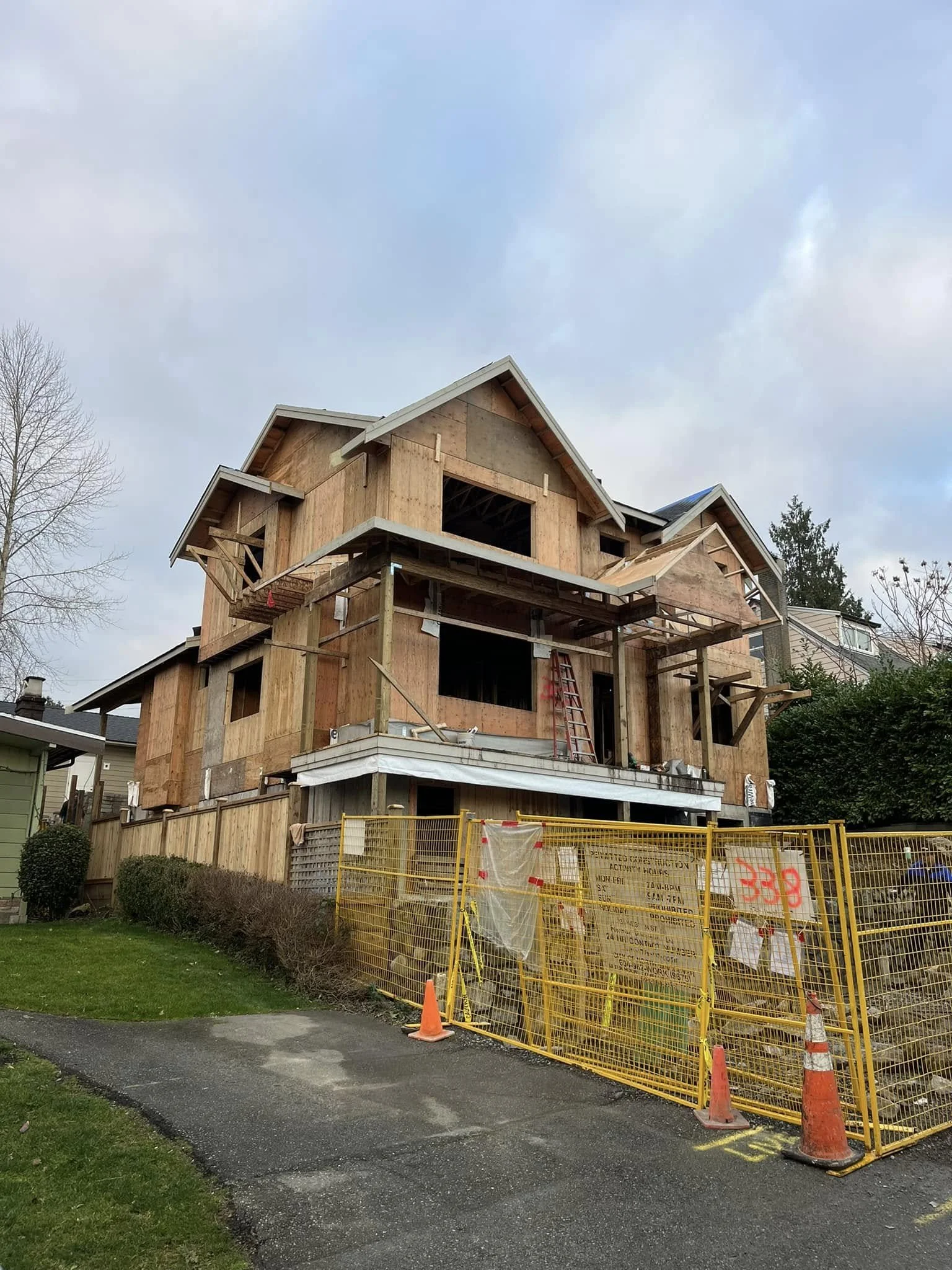 A house under construction with wooden framing, scaffolding, and construction fencing around the yard.