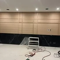 Construction site with stairs and wiring on the floor, wooden wall panels, and ceiling lights in an indoor space.