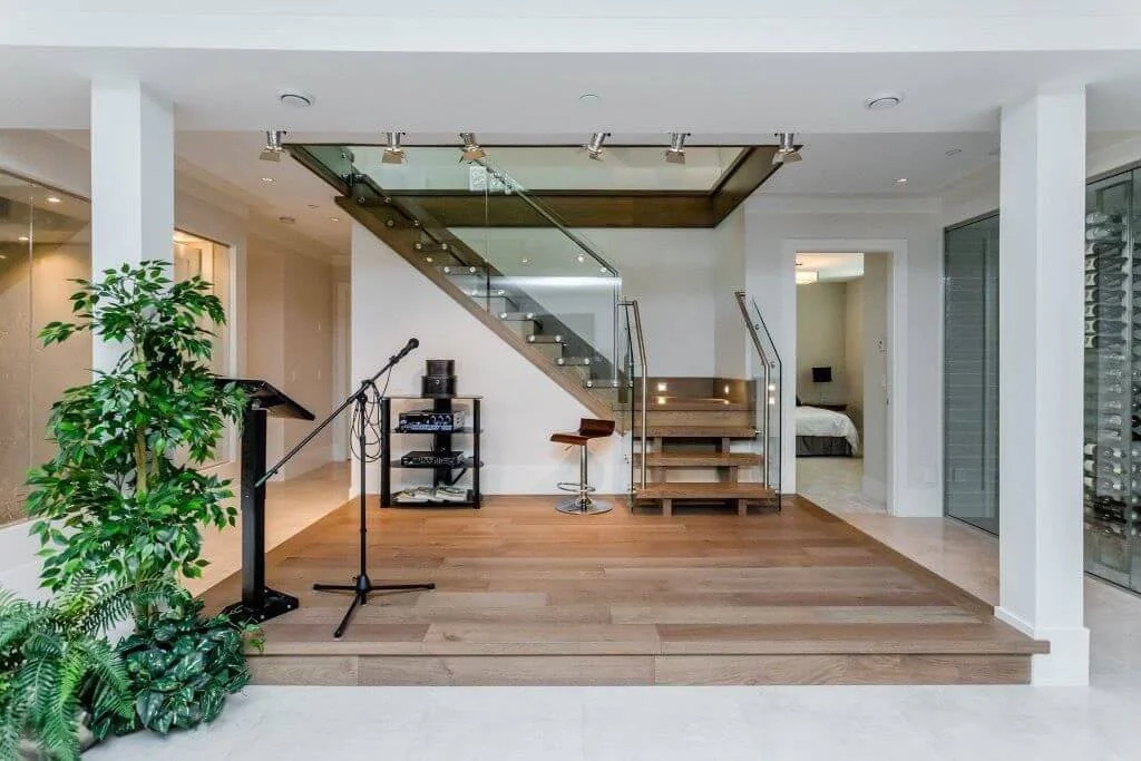 Interior of a modern house with a small stage, microphone, music equipment, staircase, and a bedroom visible in the background.